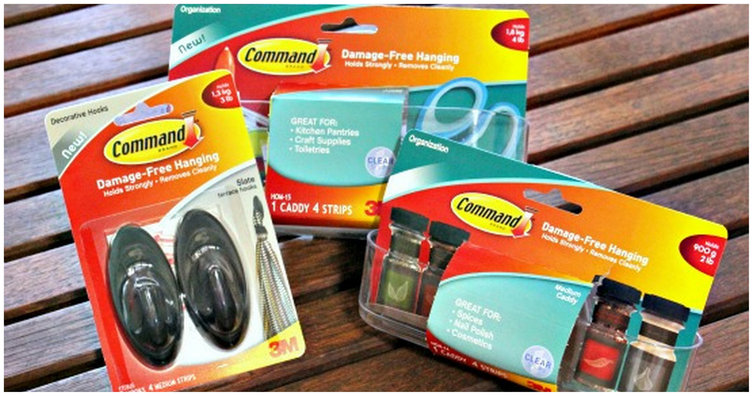 Three packages of Command brand adhesive hooks and strips resting on a slatted wood surface.