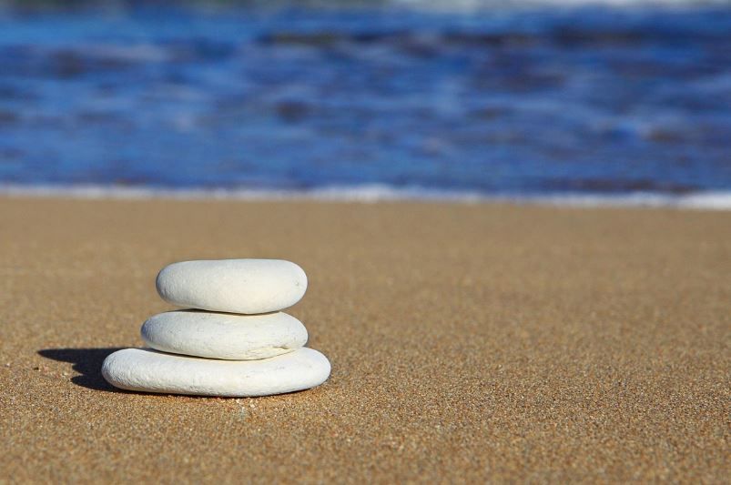 Three smooth white stones stacked on sand, urn choice reflection, cremation services Westminster, MD