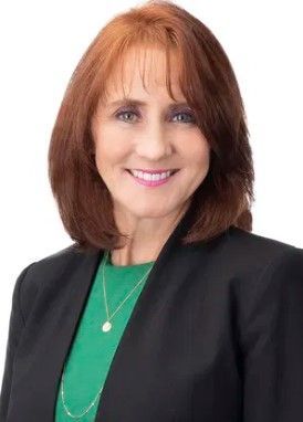 A woman wearing a black jacket and a green shirt is smiling for the camera.