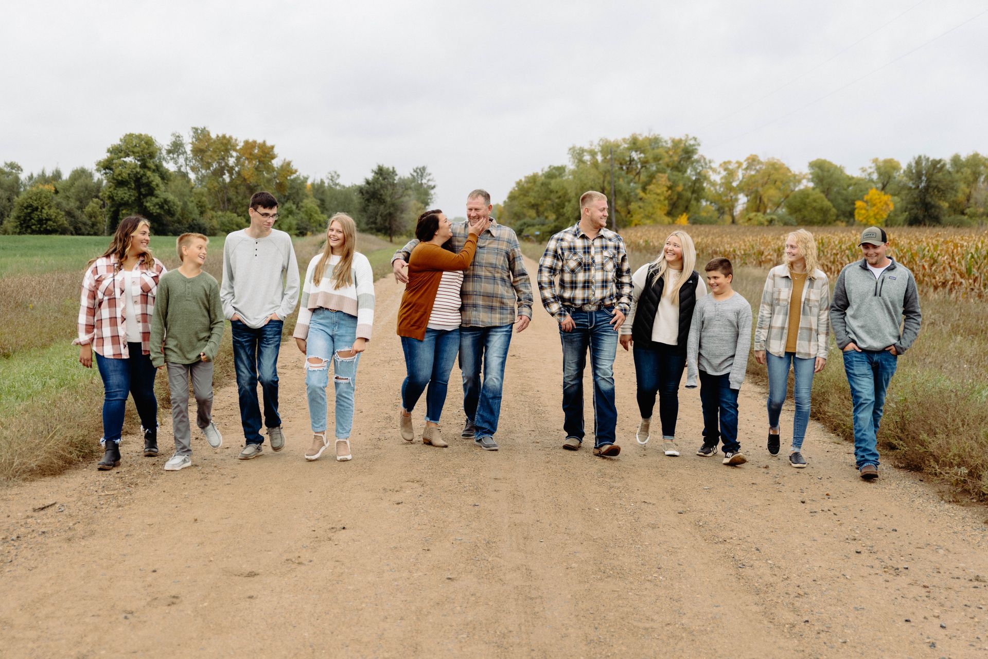 Family walking on a dirt road. People wearing casual clothes; field and trees in background.