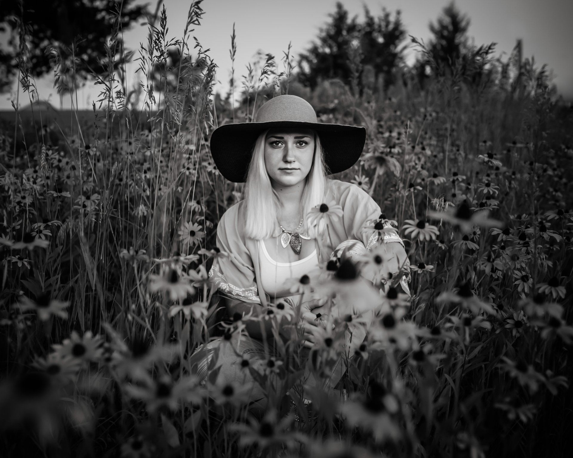 Woman in a sun hat surrounded by wildflowers; black and white photo.