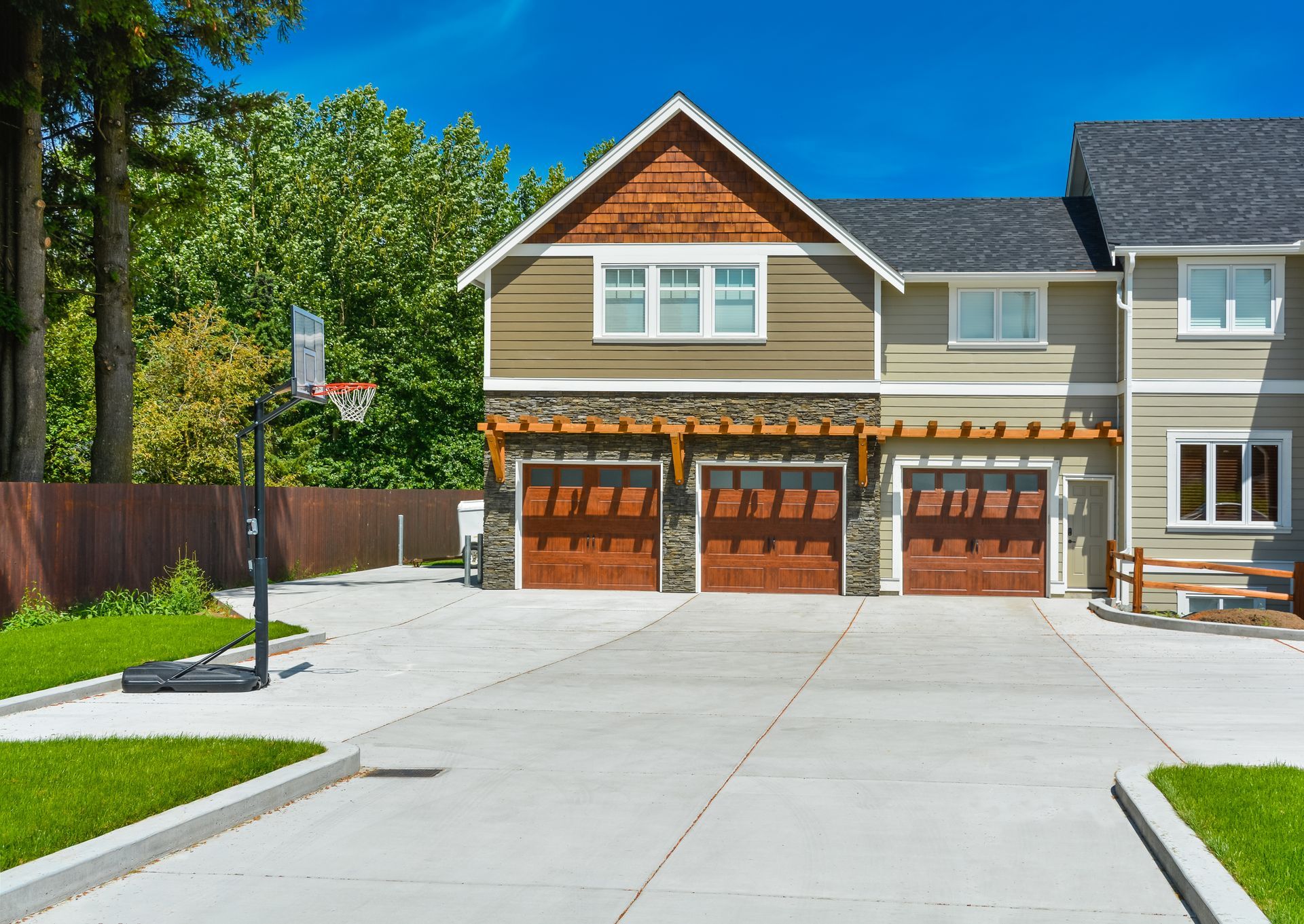 A modern house with a three-car garage and a driveway, basketball hoop in the yard.