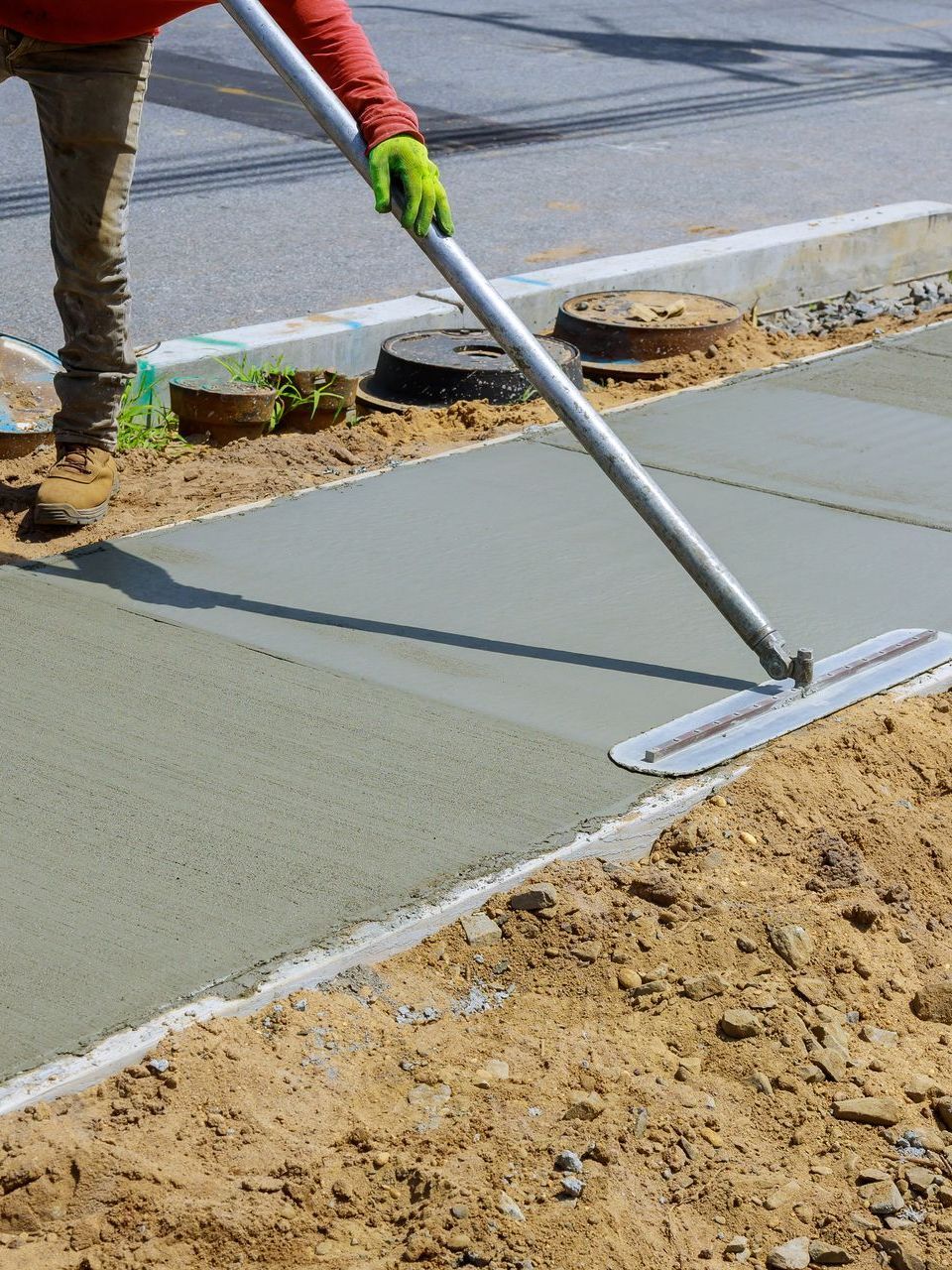 A man is spreading concrete on a sidewalk with a broom.