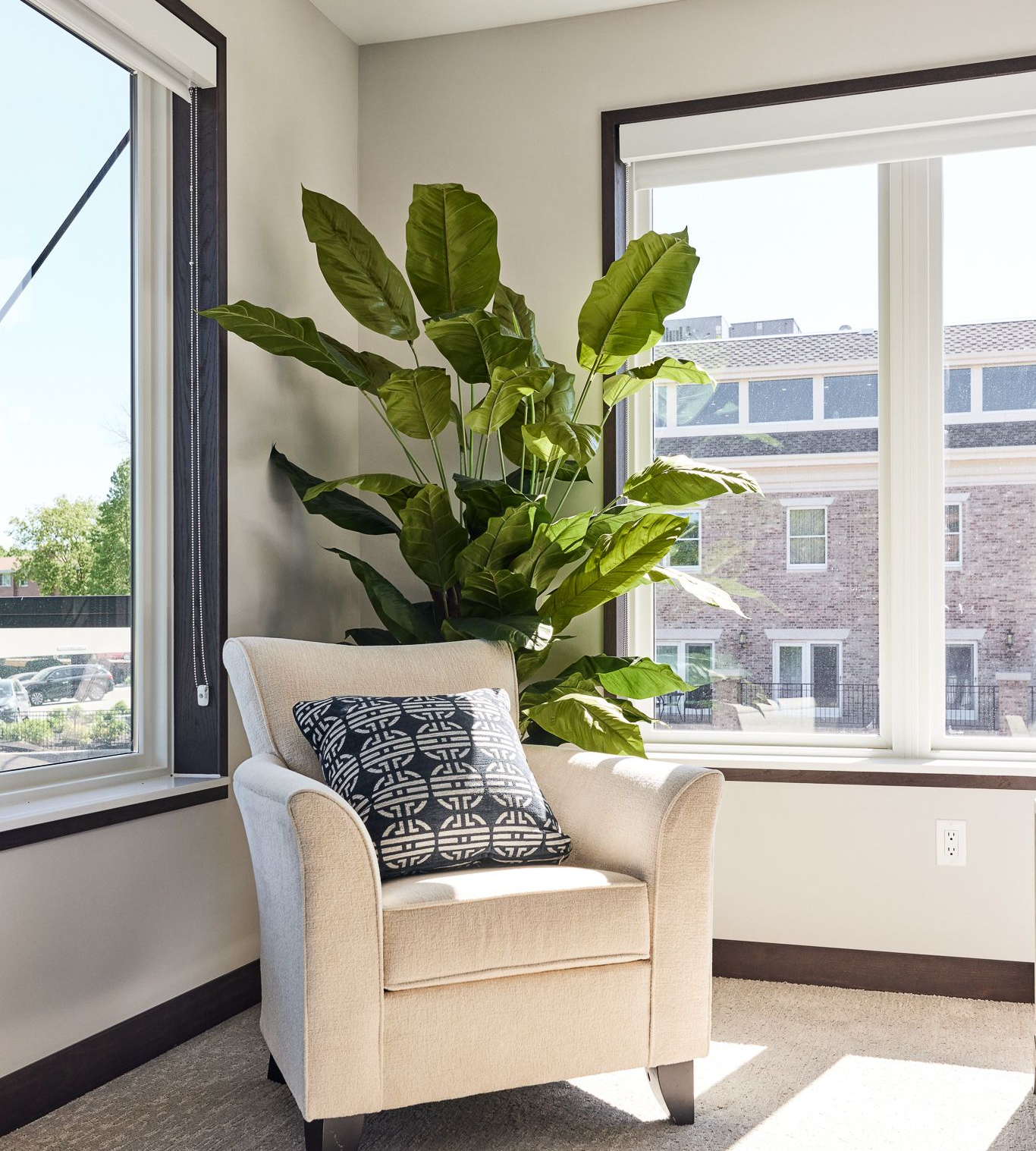Beige armchair with a decorative pillow, next to large green plant and windows at Ventana Apartments in Wayzata, MN.