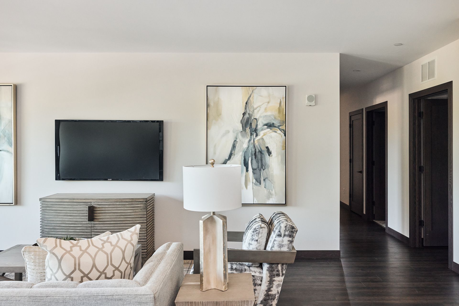 Living room with mounted TV, art, lamp, and neutral-toned furniture. Hallway with dark doors and floor visible at Ventana Apartments in Wayzata, MN.