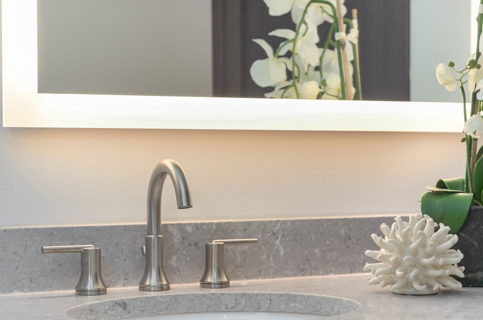 Modern bathroom sink with silver faucet, lit mirror, and decorative coral at Ventana Apartments in Wayzata, MN.