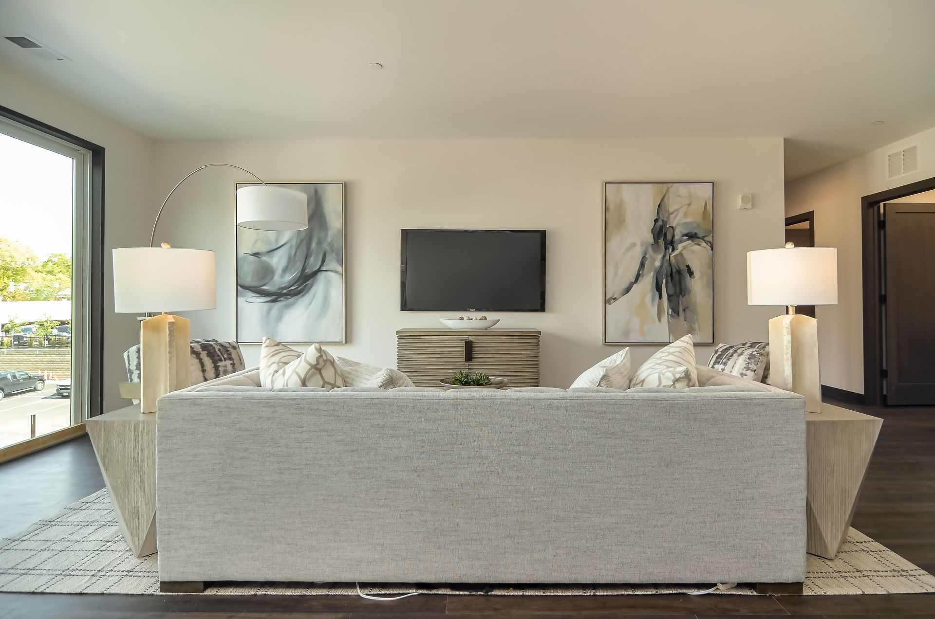 Living room with light gray sofa, artwork, TV, lamps, and dark wood floors at Ventana Apartments in Wayzata, MN.