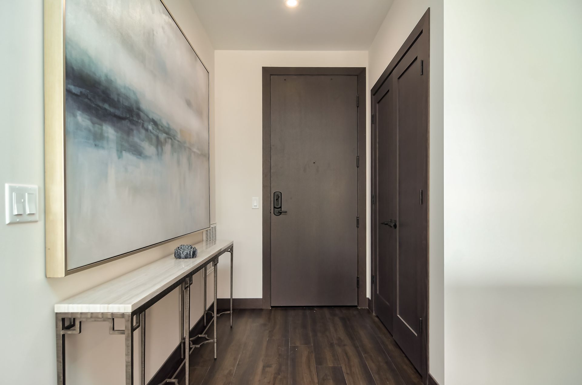 Hallway with gray door, console table, artwork, and dark wood flooring at Ventana Apartments in Wayzata, MN.