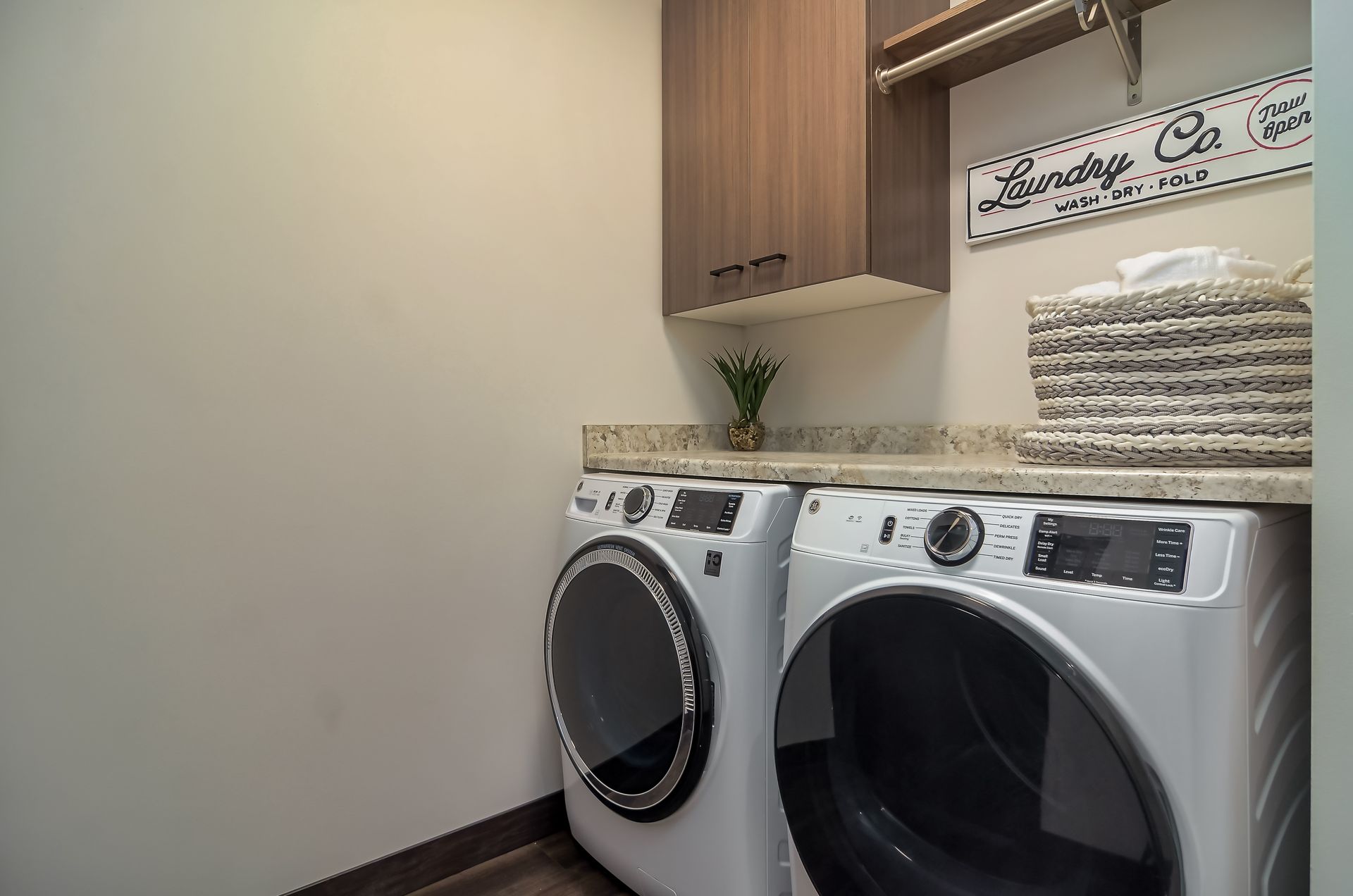 Laundry room with a washing machine, dryer, storage cabinet, and laundry basket at Ventana Apartments in Wayzata, MN.