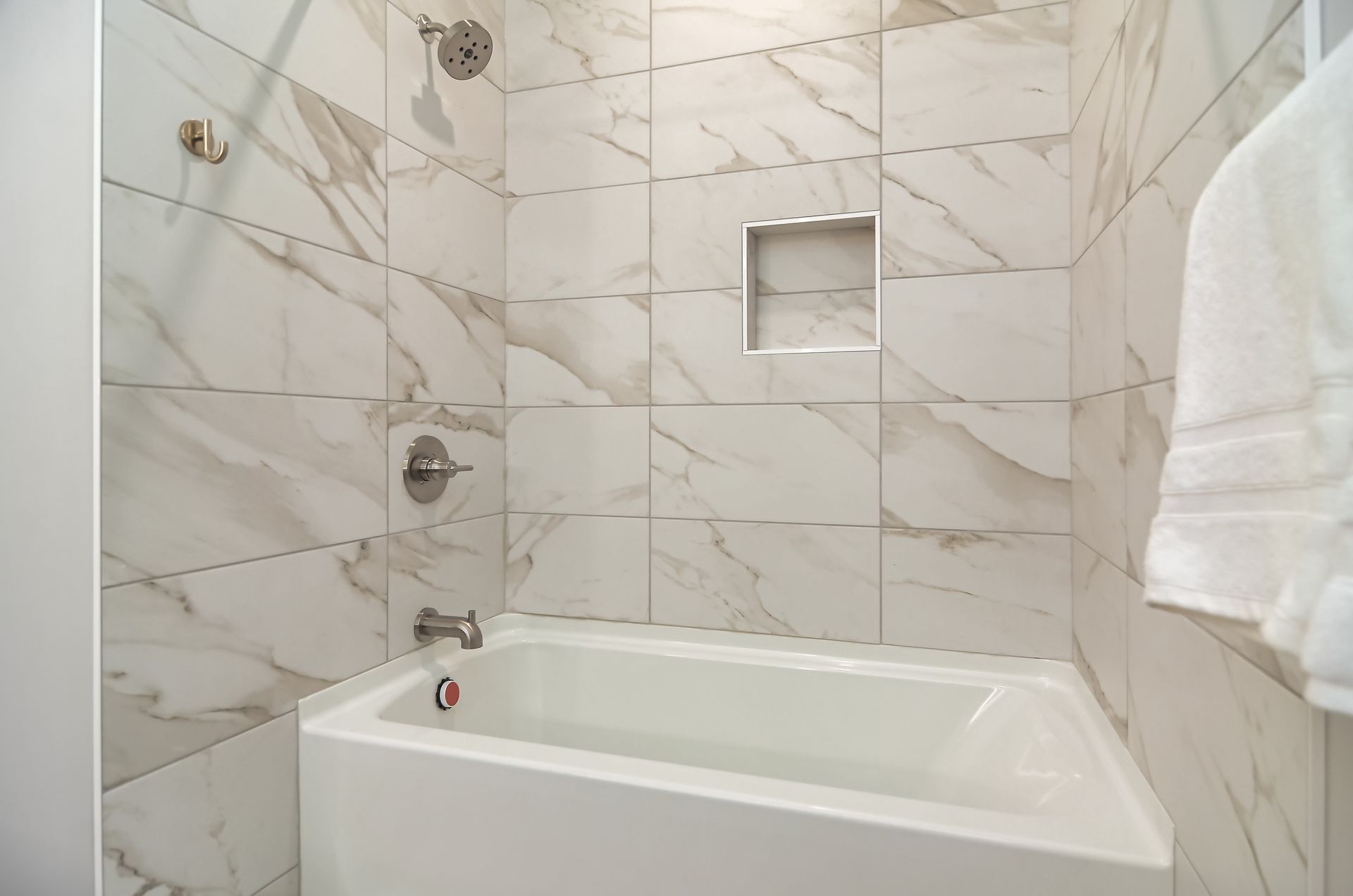White tiled bathroom with a bathtub, showerhead, and a towel hanging on the right at Ventana Apartments in Wayzata, MN.
