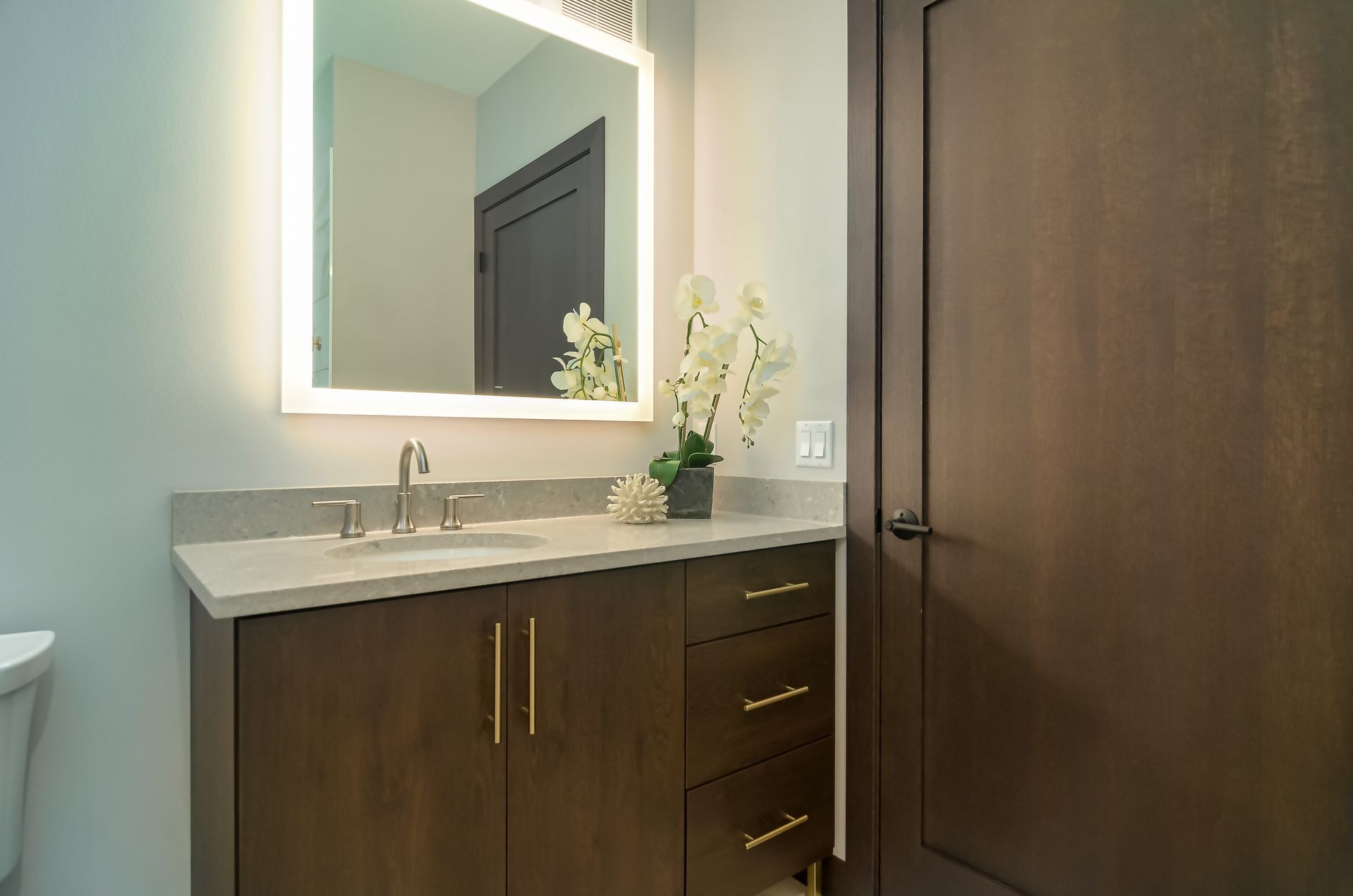 Bathroom vanity with a lighted mirror, brown cabinets, and a white countertop at Ventana Apartments in Wayzata, MN.