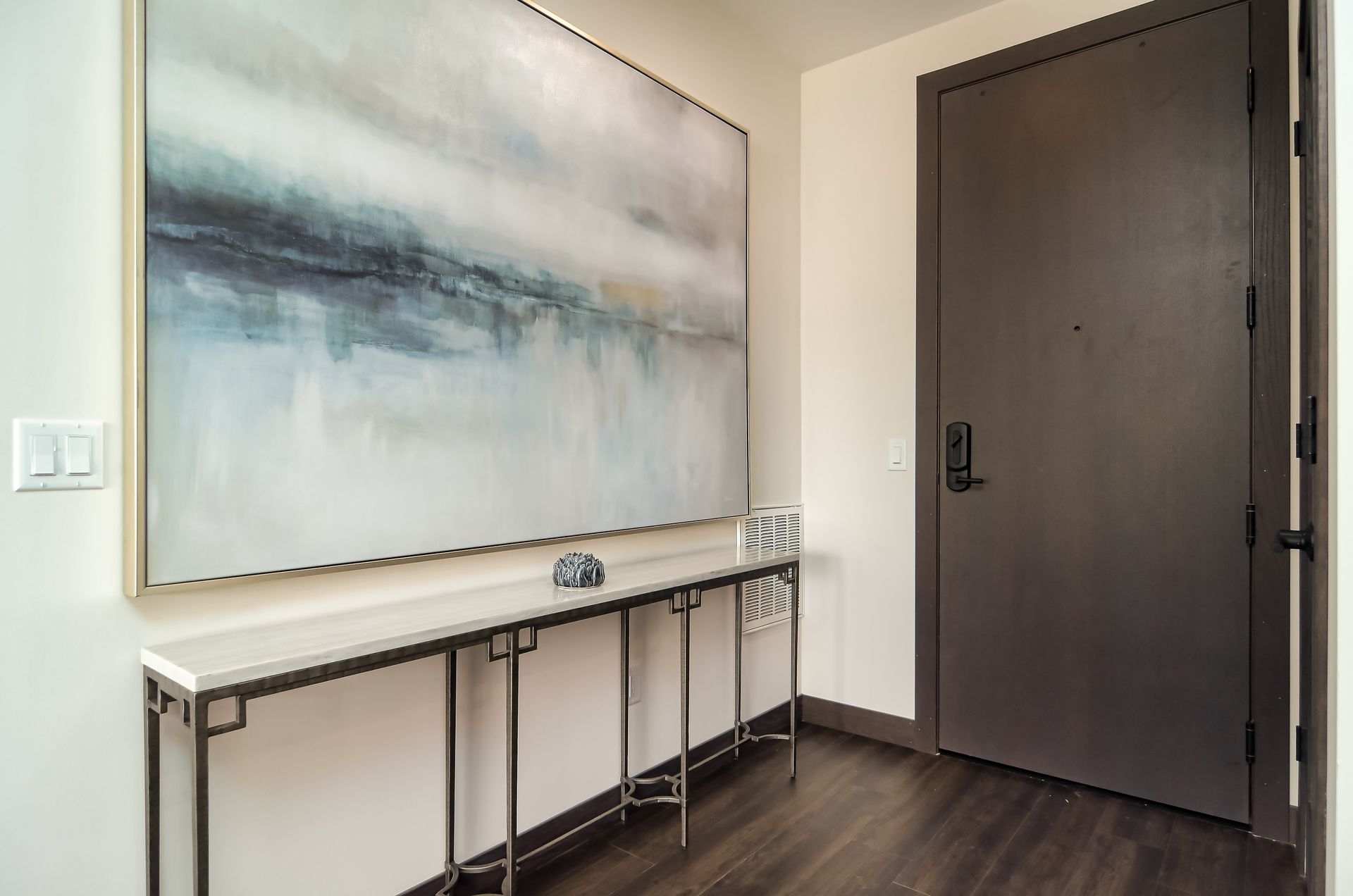 Entryway with abstract painting above a console table and a dark brown door at Ventana Apartments in Wayzata, MN.