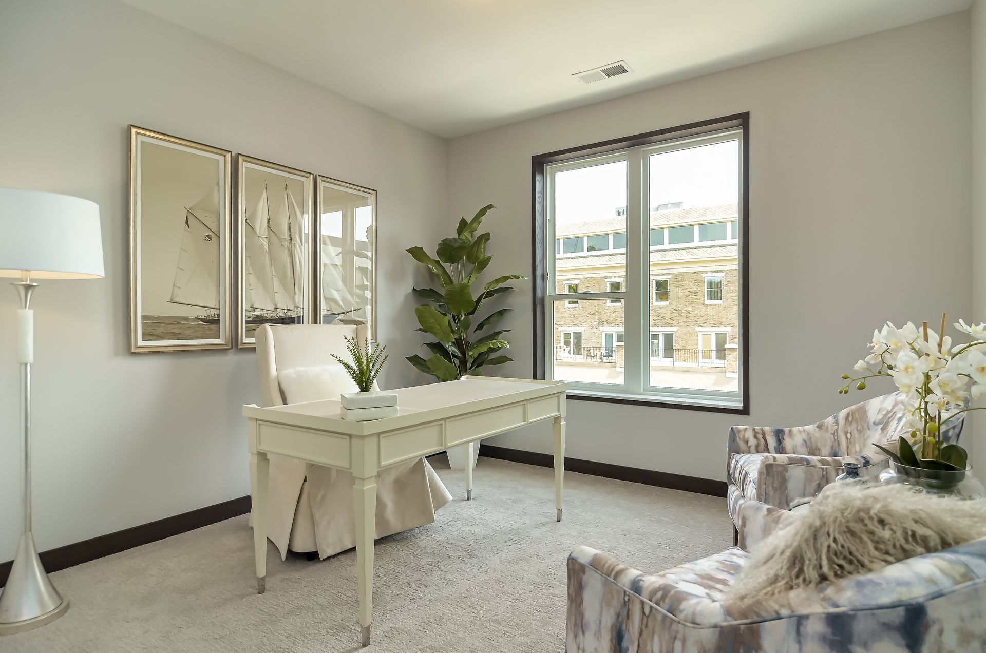 Office with desk, armchair, floor lamp, mirrors, and large window; neutral colors at Ventana Apartments in Wayzata, MN.