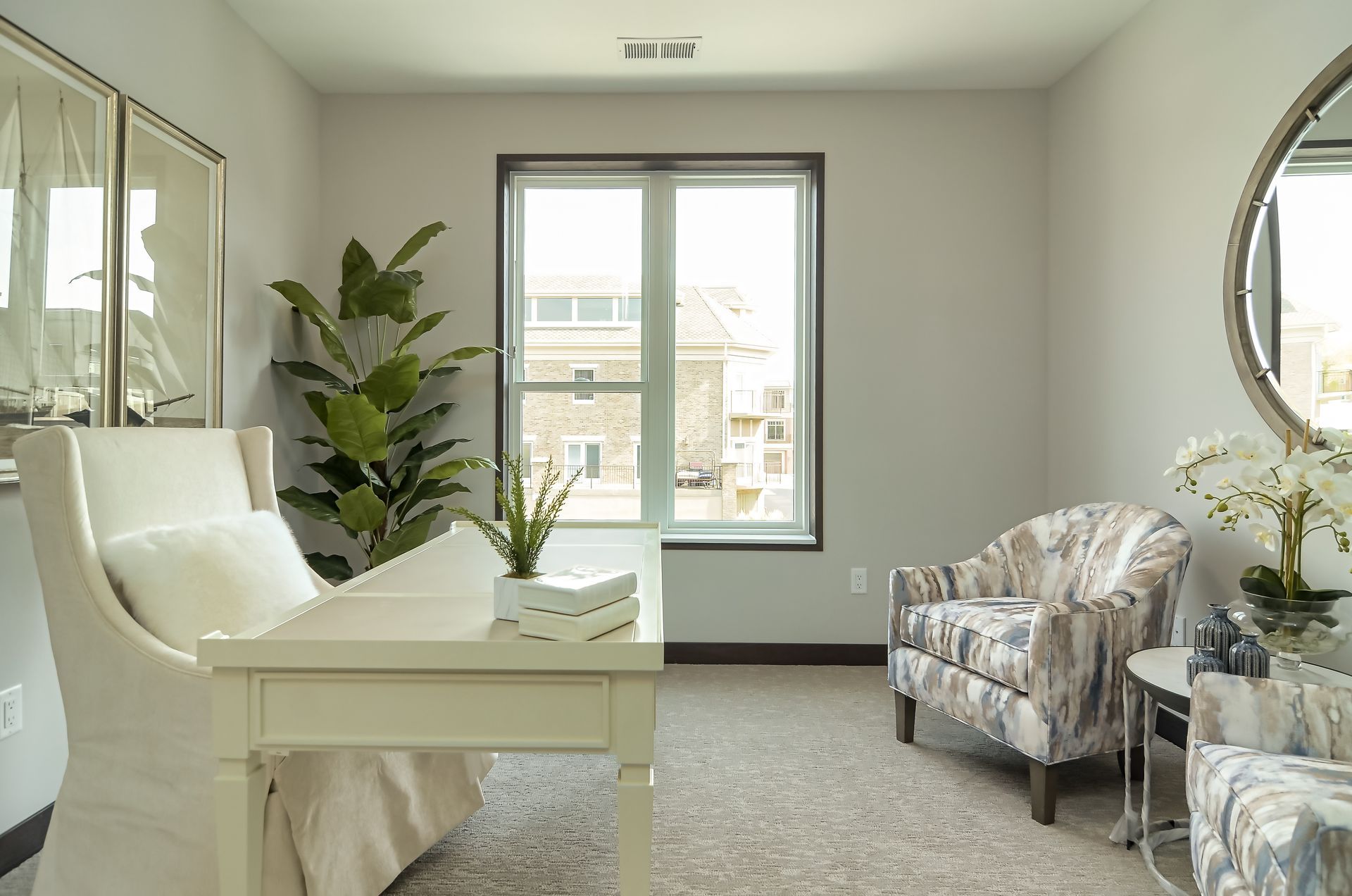 Light-filled home office with white desk, patterned armchairs, tall plant, and framed art. Window offers an outside view at Ventana Apartments in Wayzata, MN.