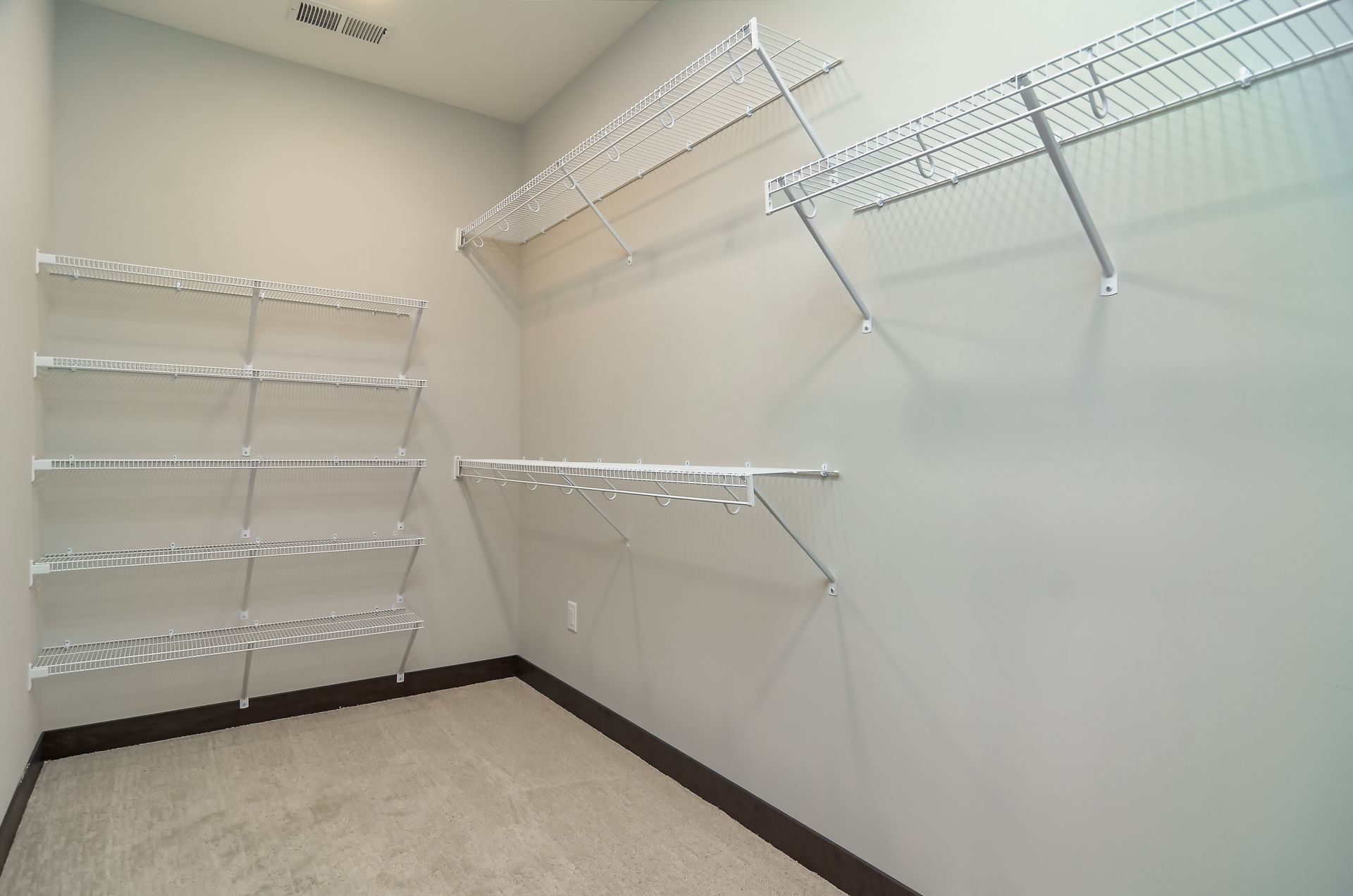 Empty walk-in closet with wire shelving on gray walls, beige carpet, and a dark brown baseboard at Ventana Apartments in Wayzata, MN.