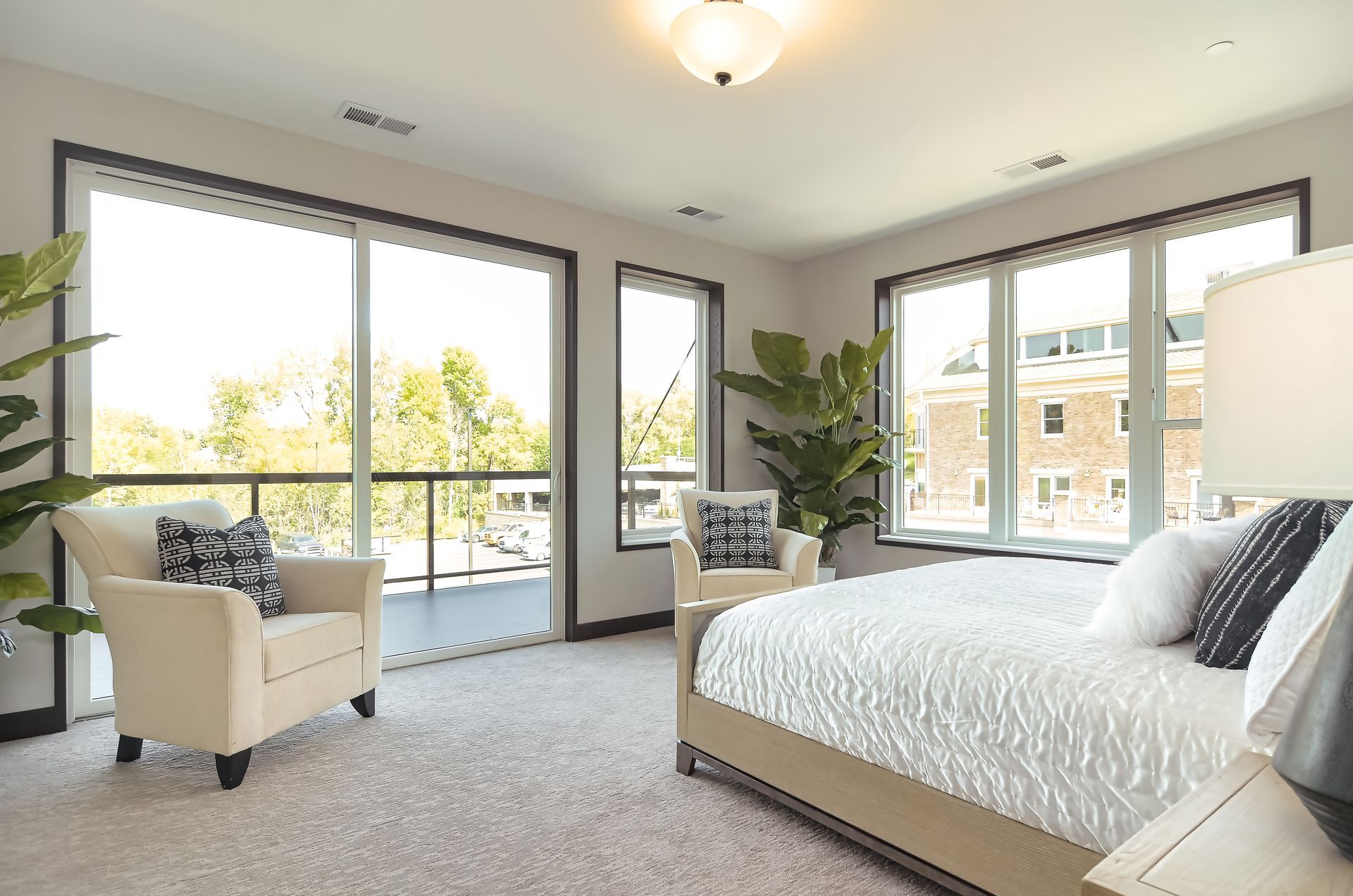 Bright bedroom with large windows, cream-colored armchair, and a bed with white bedding at Ventana Apartments in Wayzata, MN.