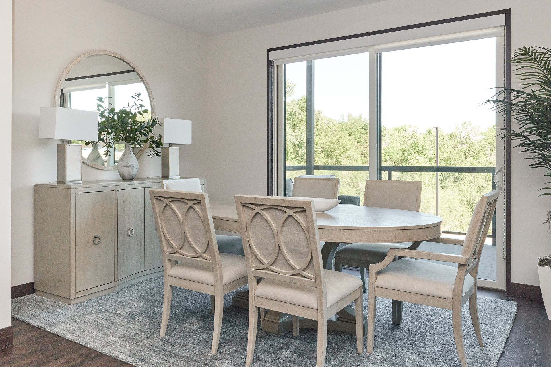 Dining room with round table, six chairs, buffet with mirror, rug, and large window with view at Ventana Apartments in Wayzata, MN.