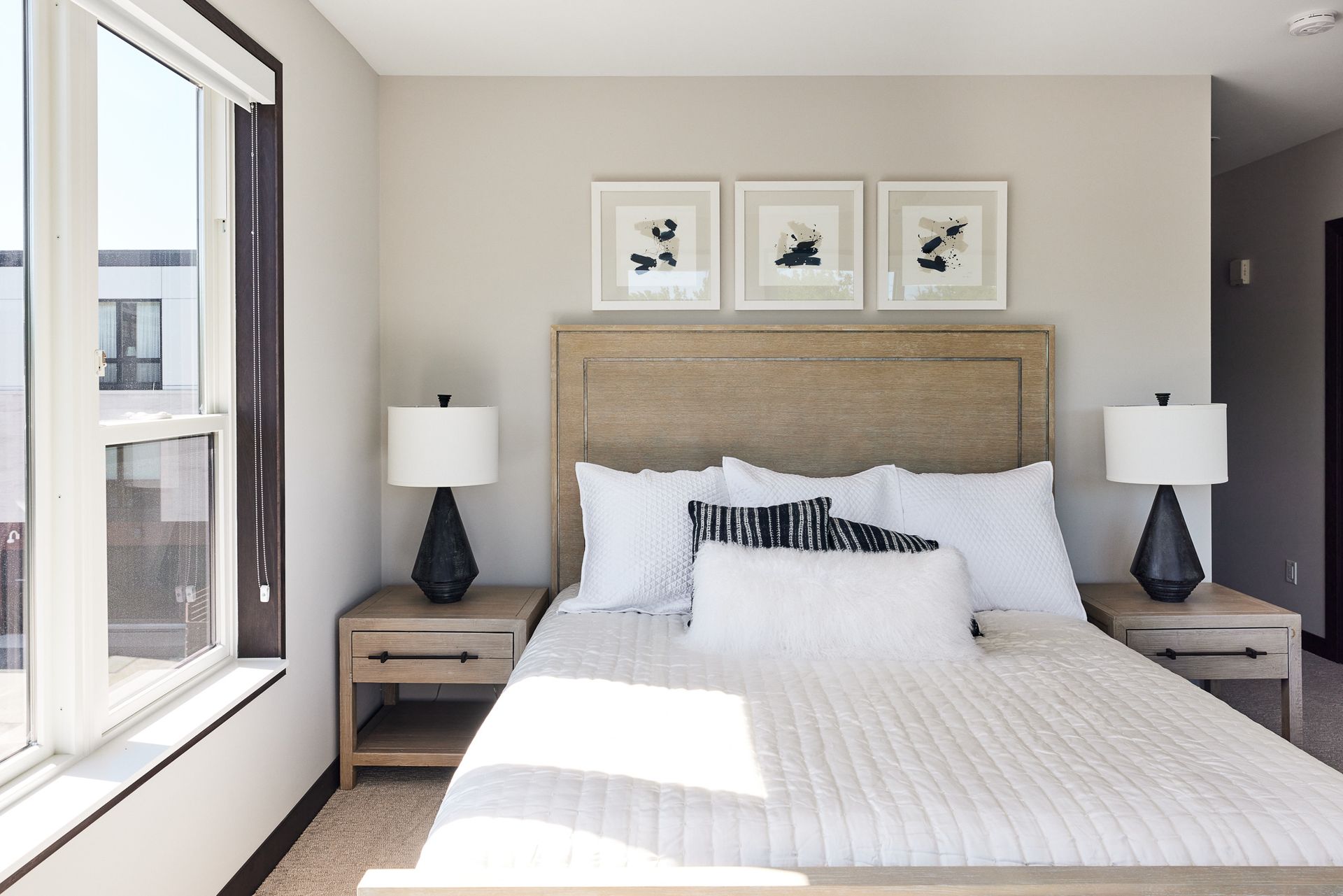 Bedroom with bed, nightstands, lamps, artwork, and large window. Neutral color scheme at Ventana Apartments in Wayzata, MN.