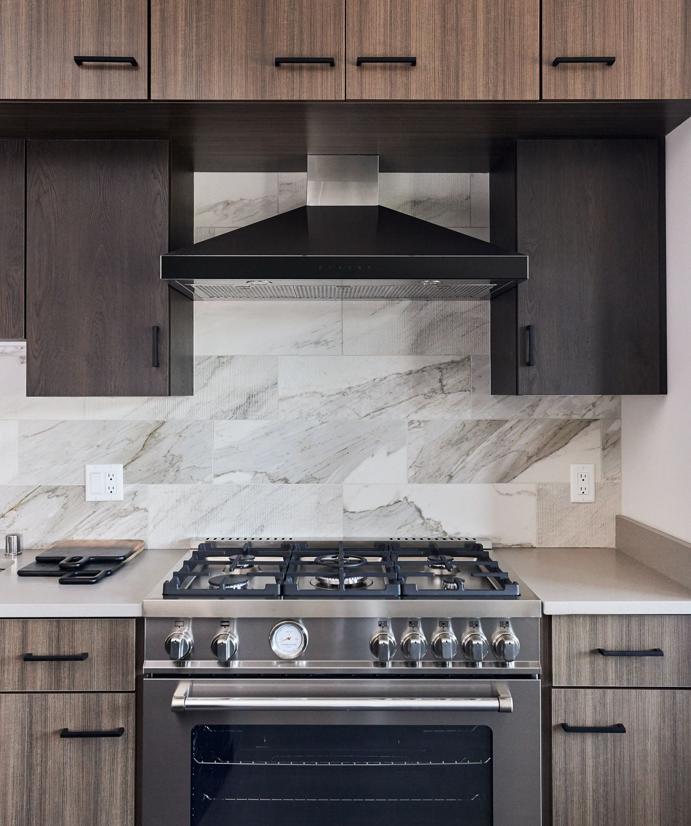 Modern kitchen with stainless steel stove, dark cabinets, marble backsplash, and range hood at Ventana Apartments in Wayzata, MN.