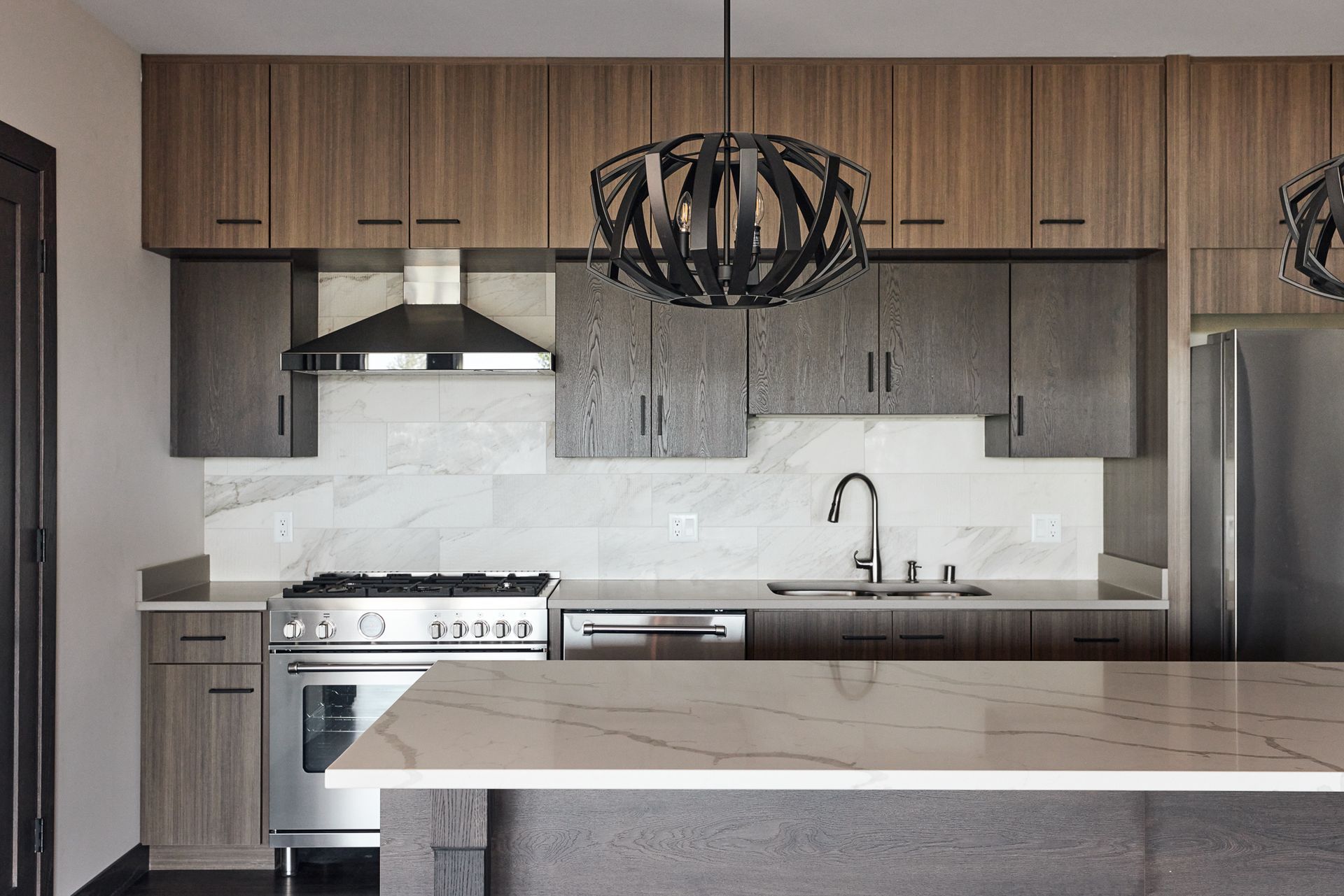 Modern kitchen with wood and gray cabinets, stainless steel appliances, and a marble countertop at Ventana Apartments in Wayzata, MN.