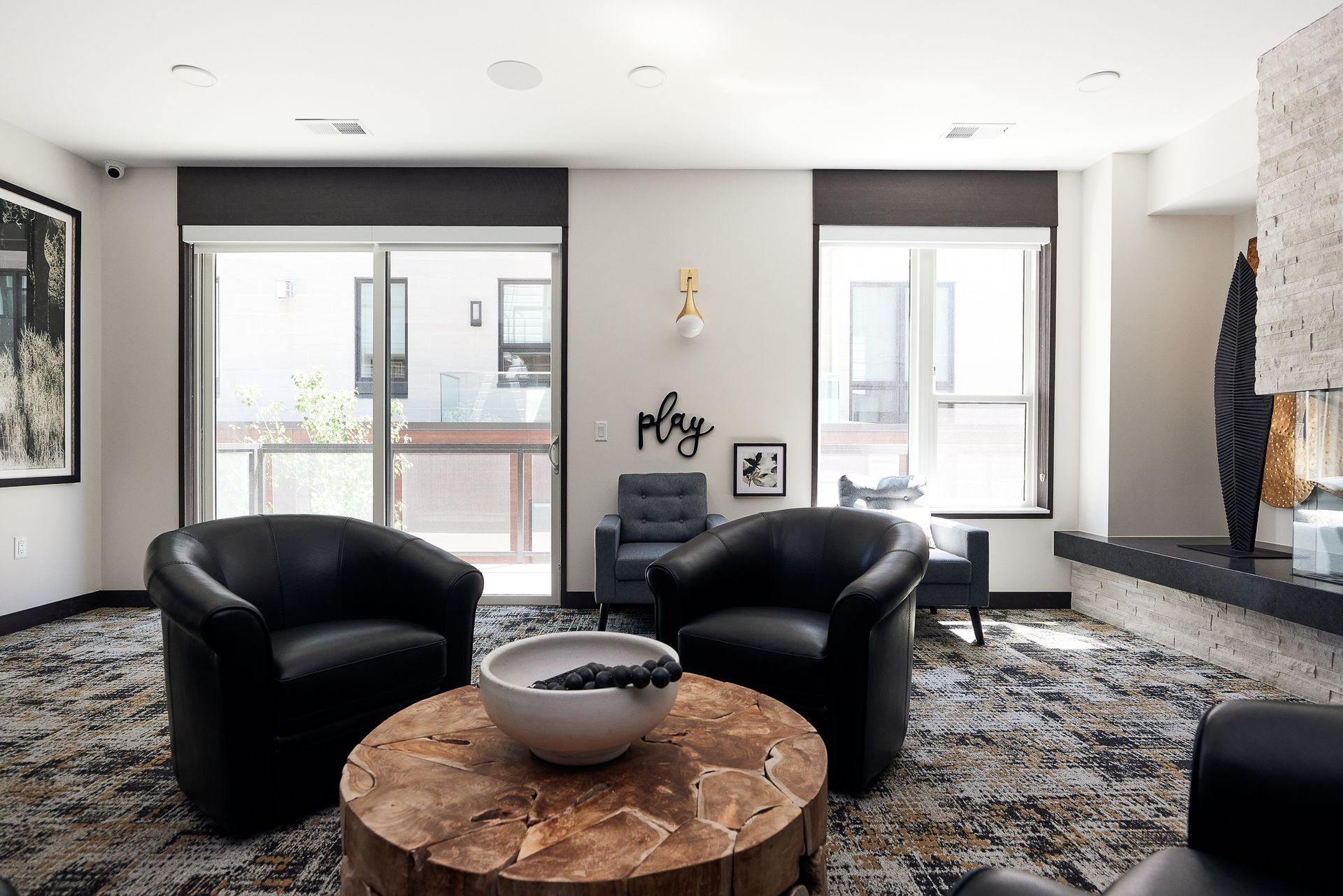 Modern living room with black chairs, round wood table, patterned rug, and large windows Apartments in Wayzata, MN
