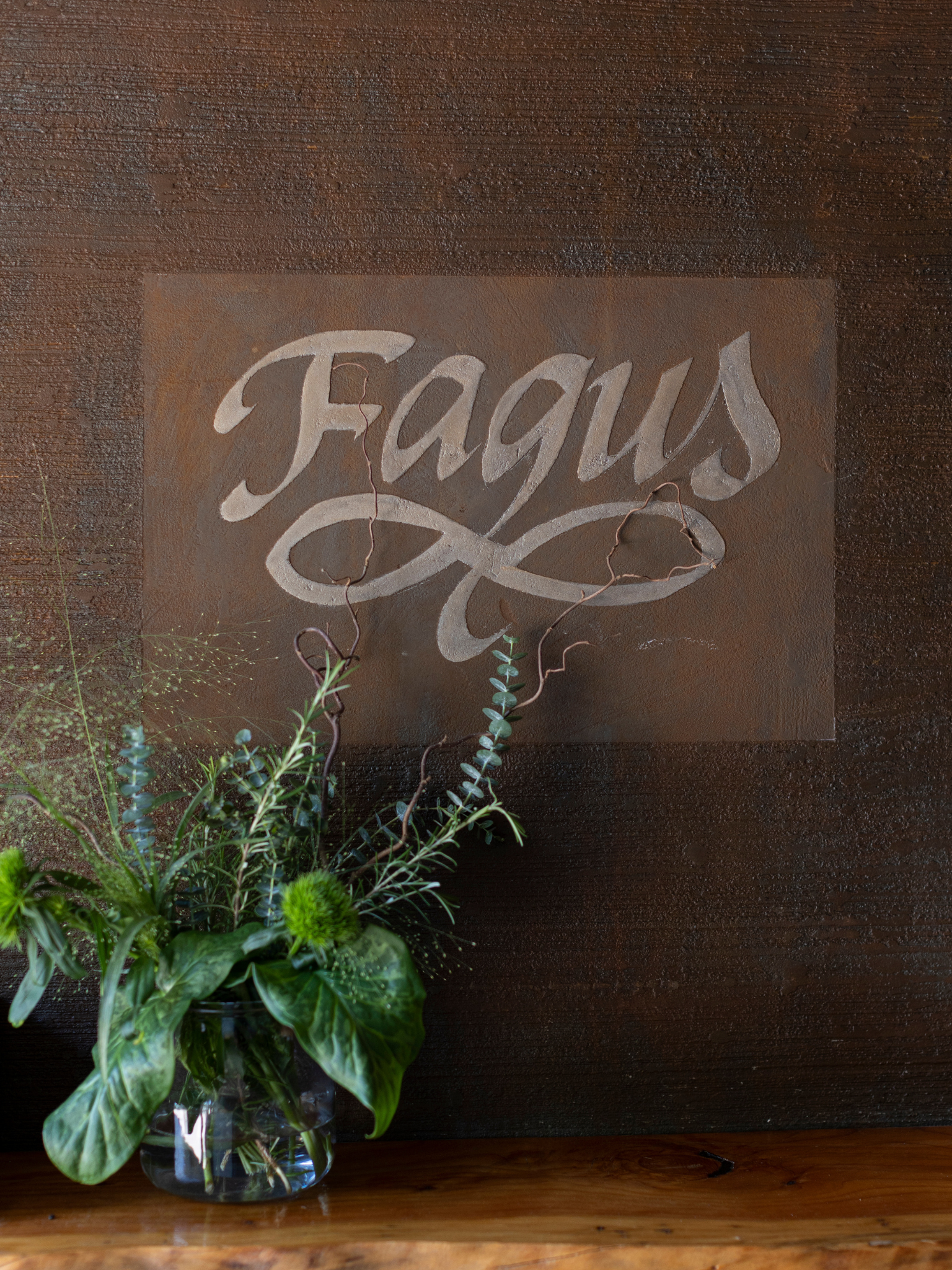 Un vaso di fiori è appoggiato su un tavolo davanti a un cartello che dice fagus.