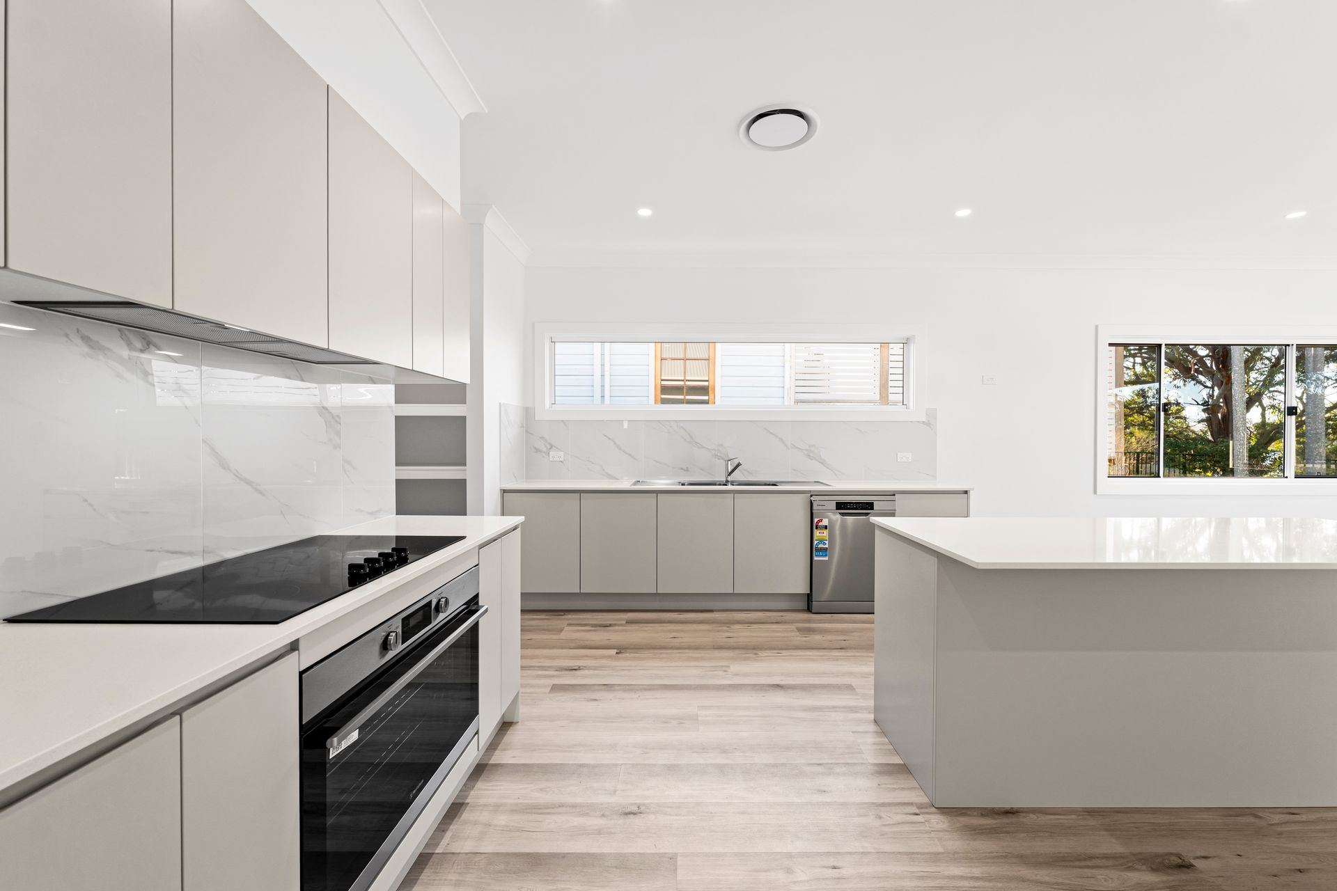 Modern Kitchen With Light Wood Floor, Gray Cabinets, White Countertops and Island, and A Window — Designer Building Pty Ltd In Erina, NSW