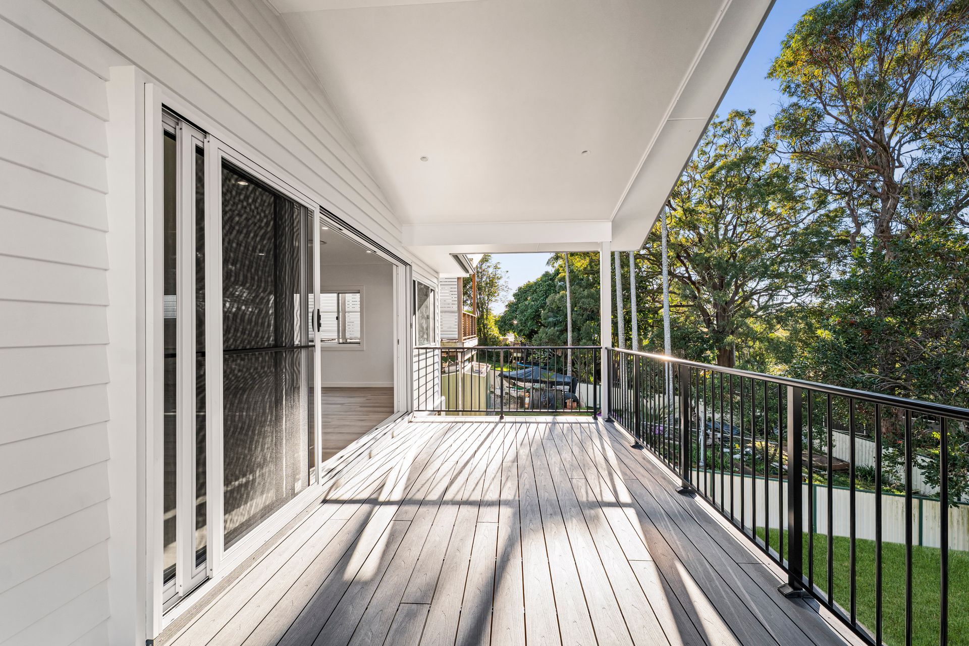 Balcony with White Wood Siding, Dark Railings, and Wooden Floor; Opens to Yard — Designer Building Pty Ltd In Charmhaven, NSW