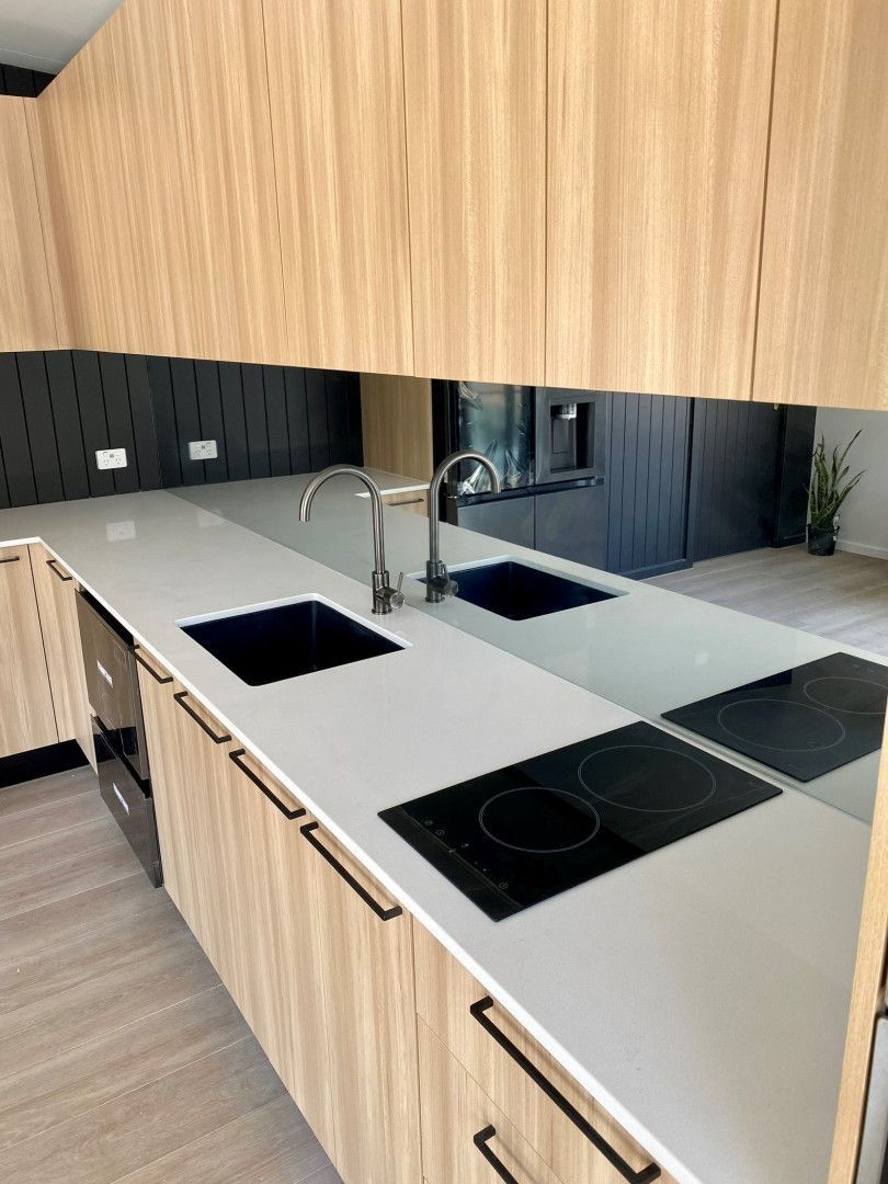Modern kitchen with light wood cabinets, white countertops, black cooktop, and mirrored backsplash — Designer Building Pty Ltd In Charmhaven, NSW