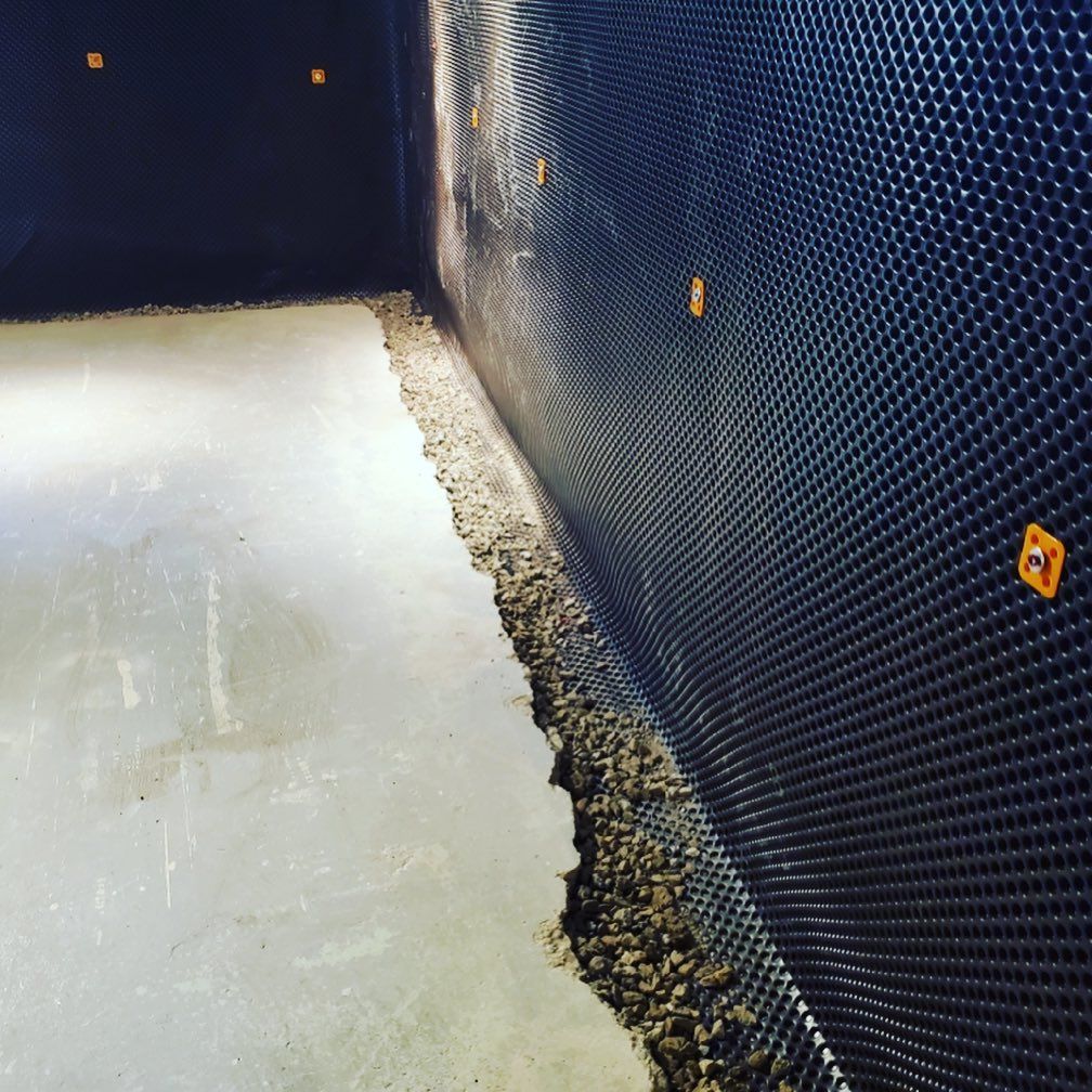 A drainage system is being installed on a wall in a basement.