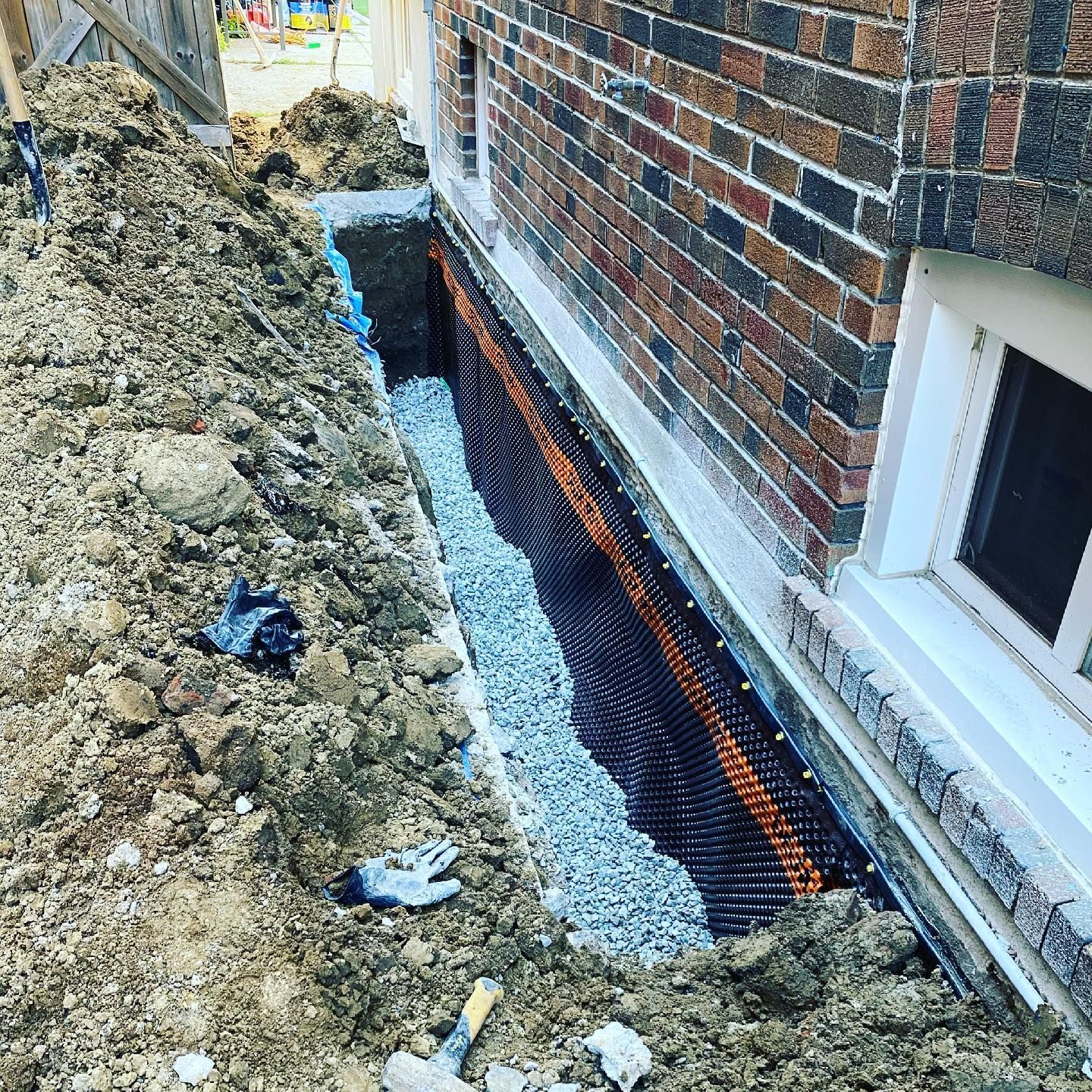 A drainage system is being installed on the side of a brick house.