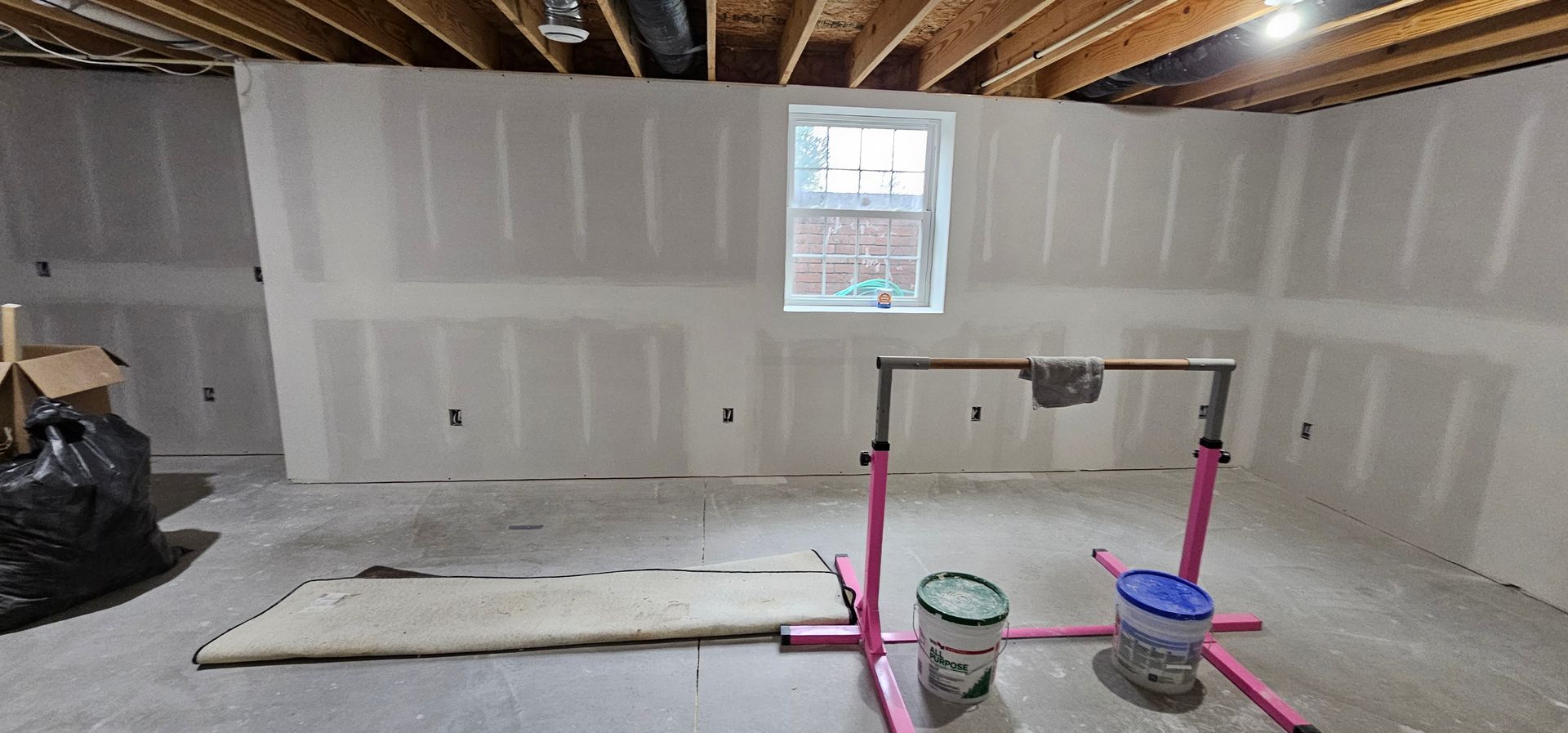 Unfinished basement with drywall, exposed beams, and construction materials on the floor