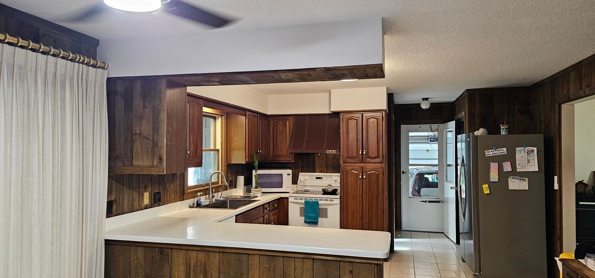 Kitchen with wood cabinets, white countertops, and a doorway to a hall with a refrigerator.