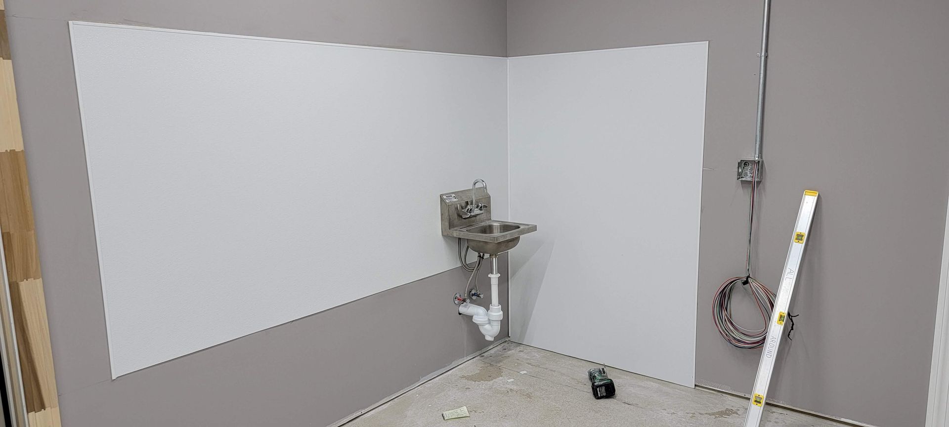 Empty room with fresh white and gray walls, a sink, and painting supplies on the floor