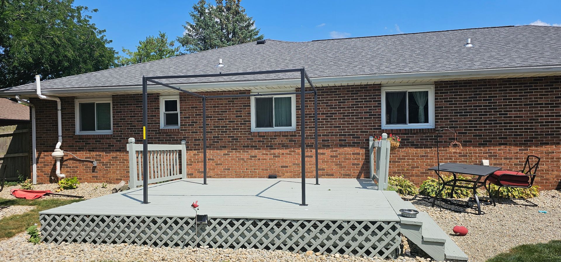 Brick house with a raised wooden deck, white railings, and a picnic table in a backyard.