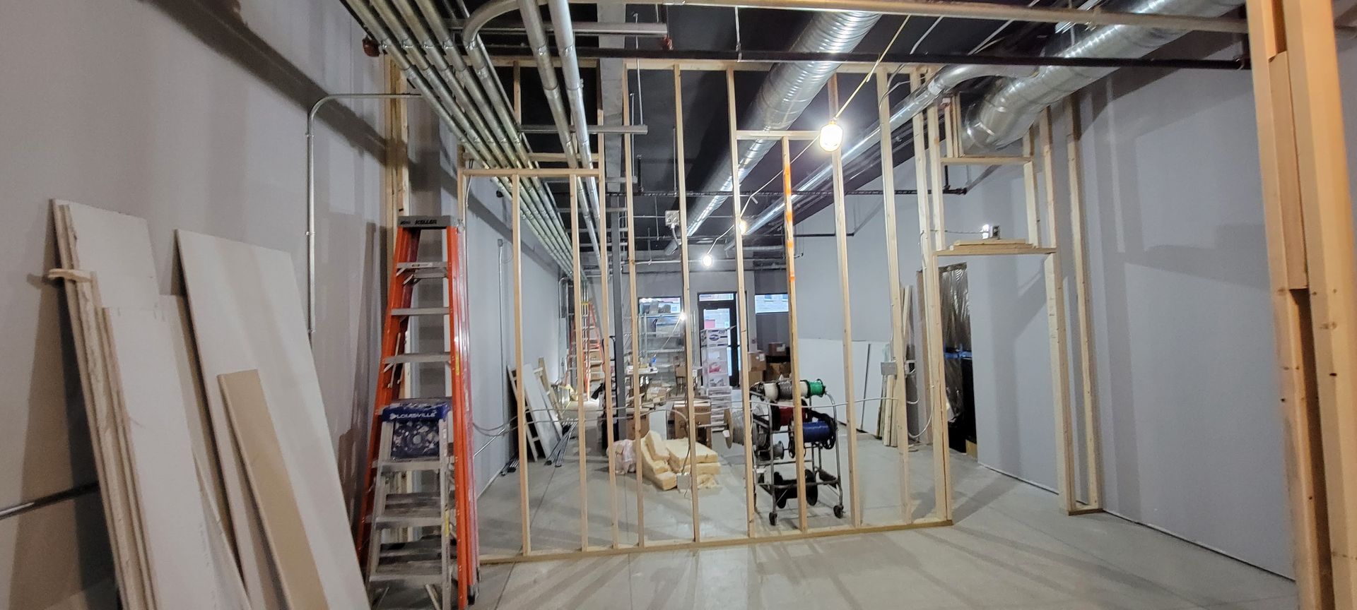 Interior of a building under construction with exposed framing, ladders, and stacked panels along a narrow hallway.