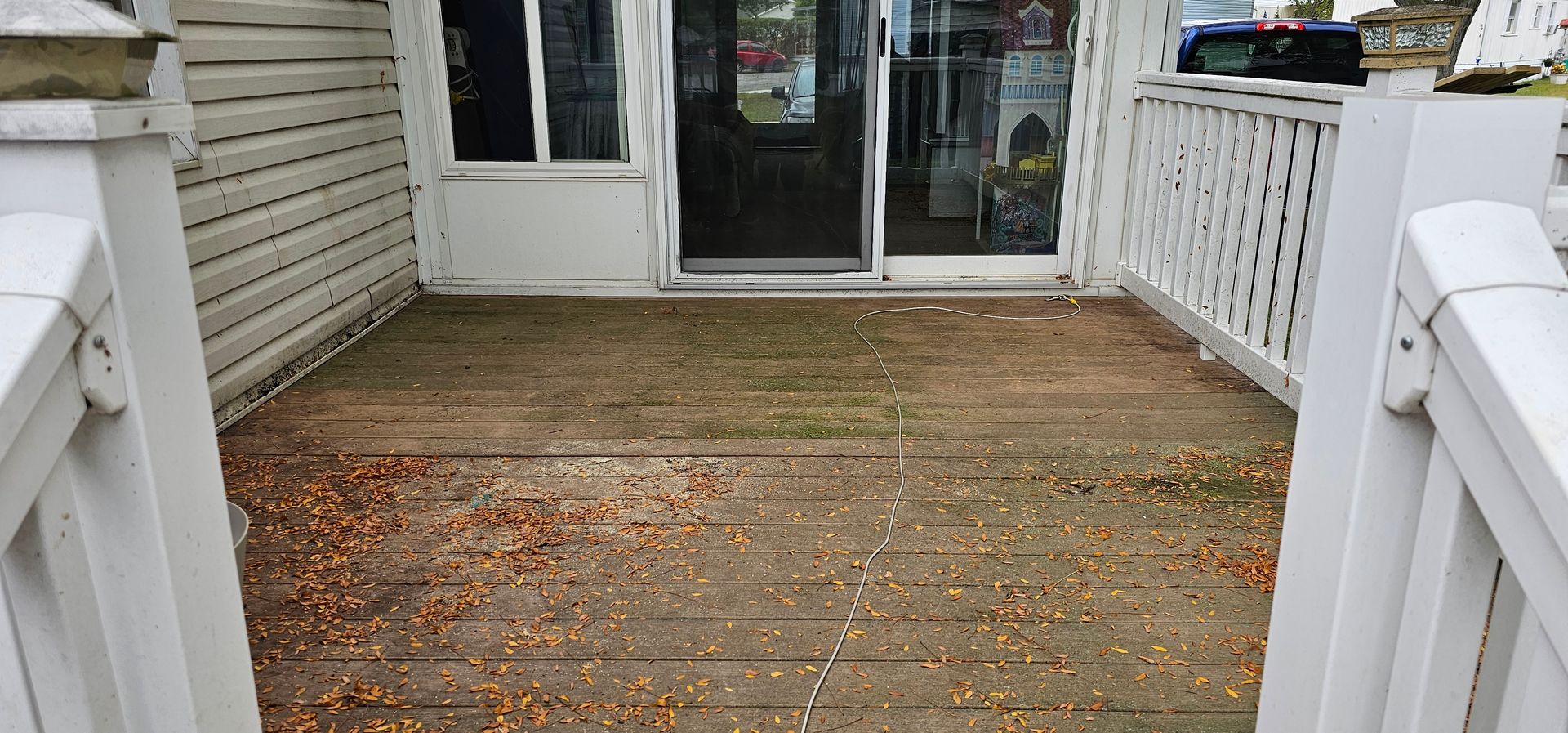 Wooden porch leading to a glass sliding door, with white railings and scattered leaves.