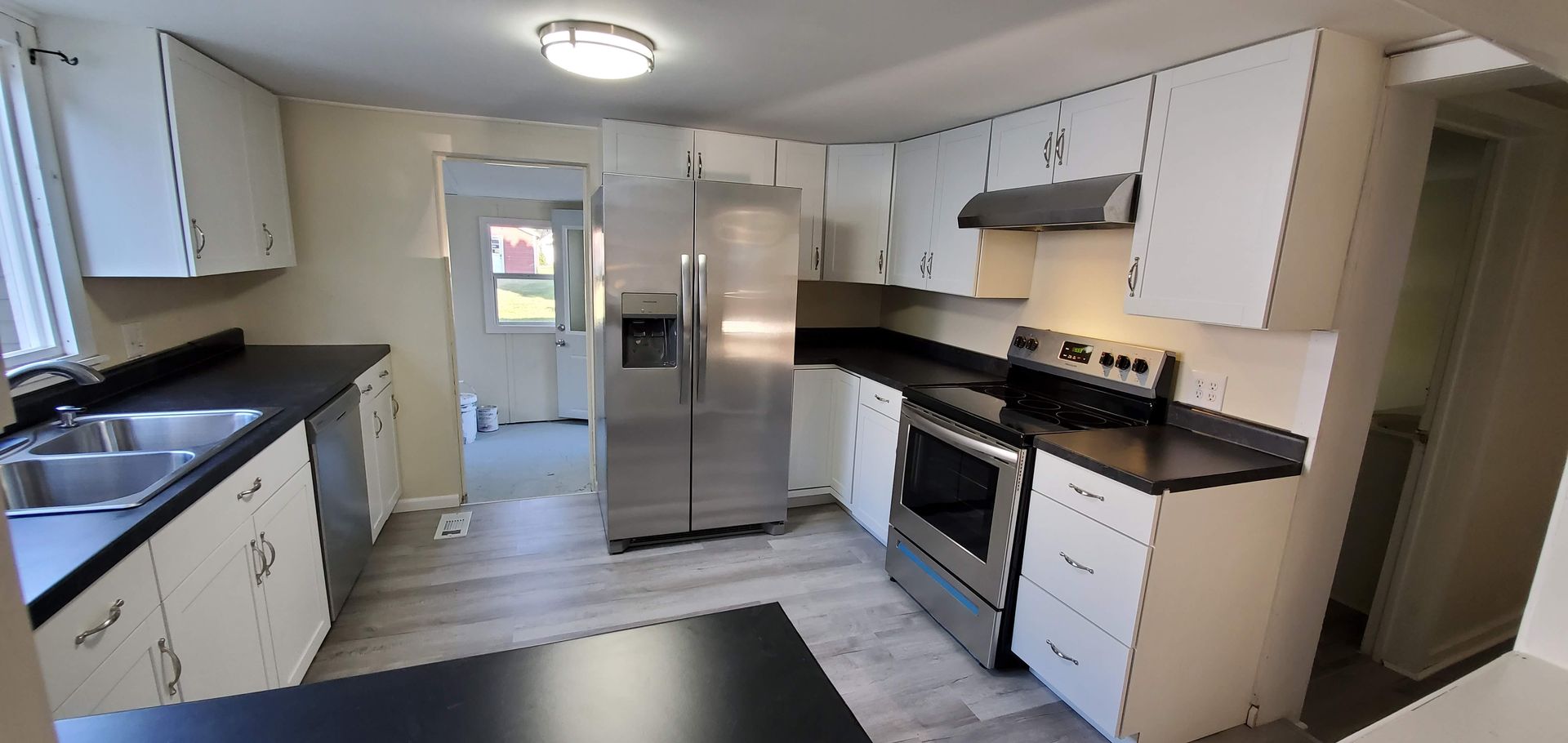 Modern kitchen with white cabinets, black countertops, stainless steel appliances, and a door at the back