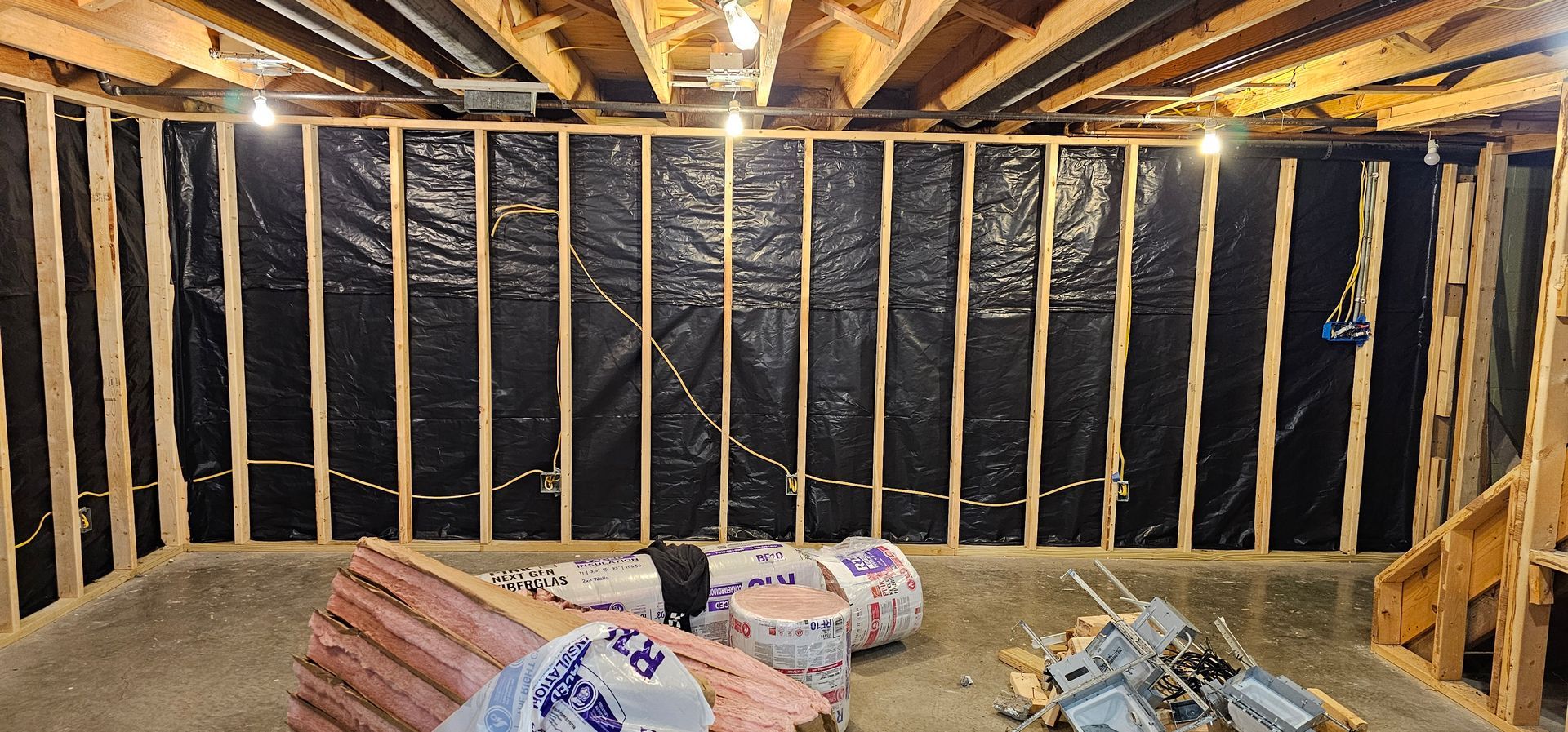 Unfinished basement wall with black insulation, exposed studs, and construction materials on the floor