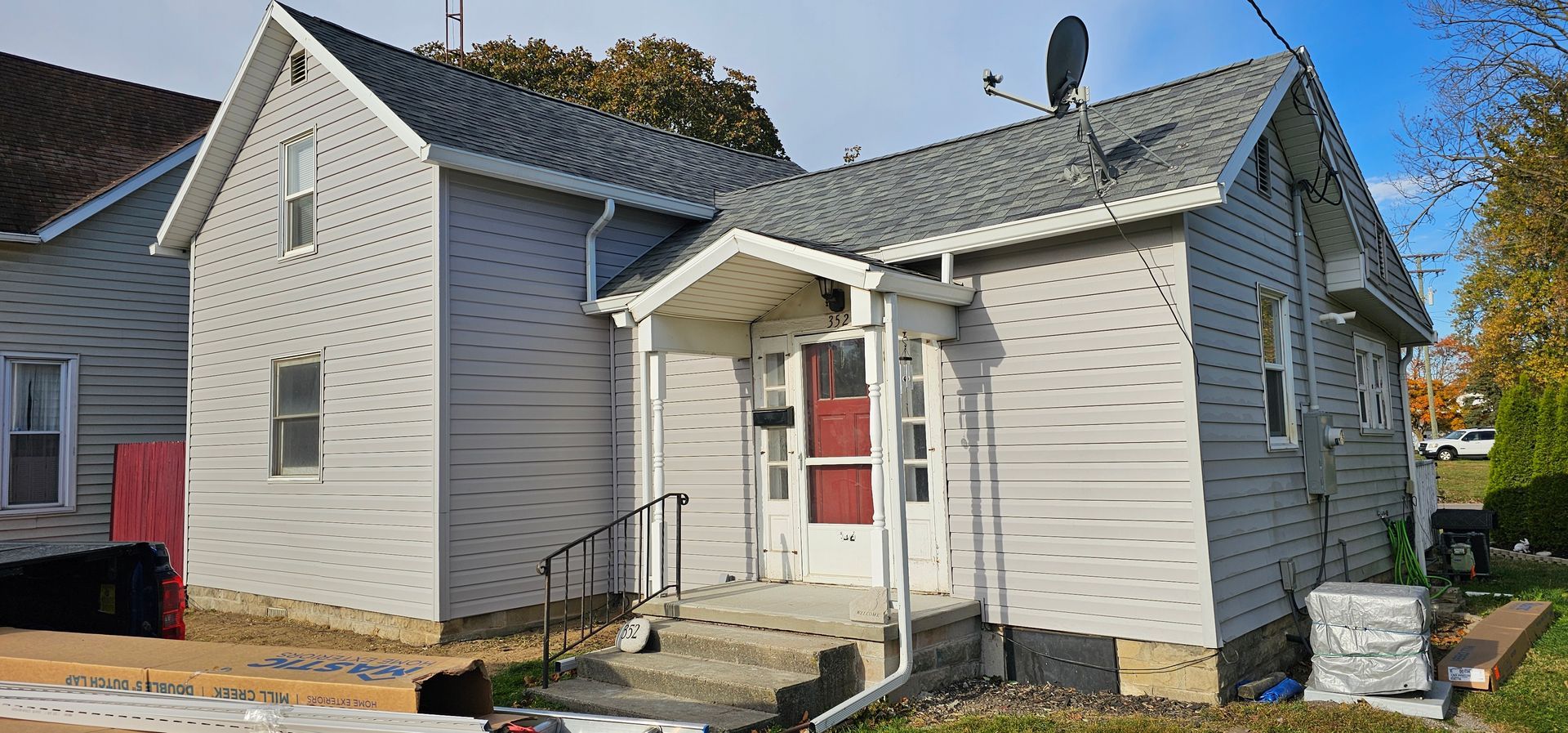 Small gray house with a red front door and white trim on a sunny street corner.