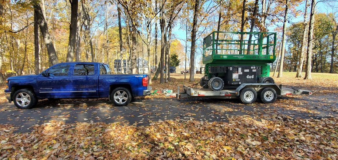 Blue pickup truck towing a green utility trailer through a leaf-covered wooded area