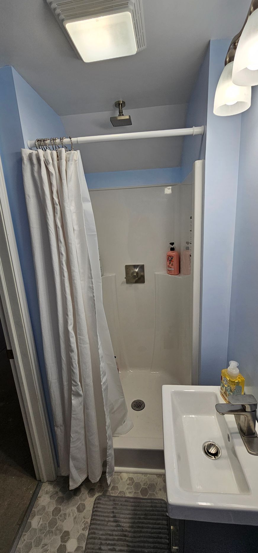 Small bathroom with shower curtain, sink, and blue walls under bright overhead lights