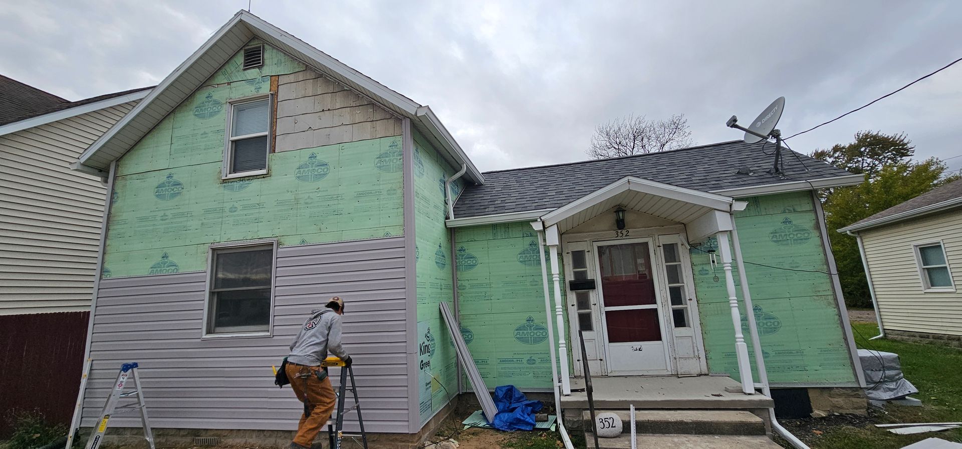 Workers painting a house exterior with green and white primer, one person on a ladder under repair.