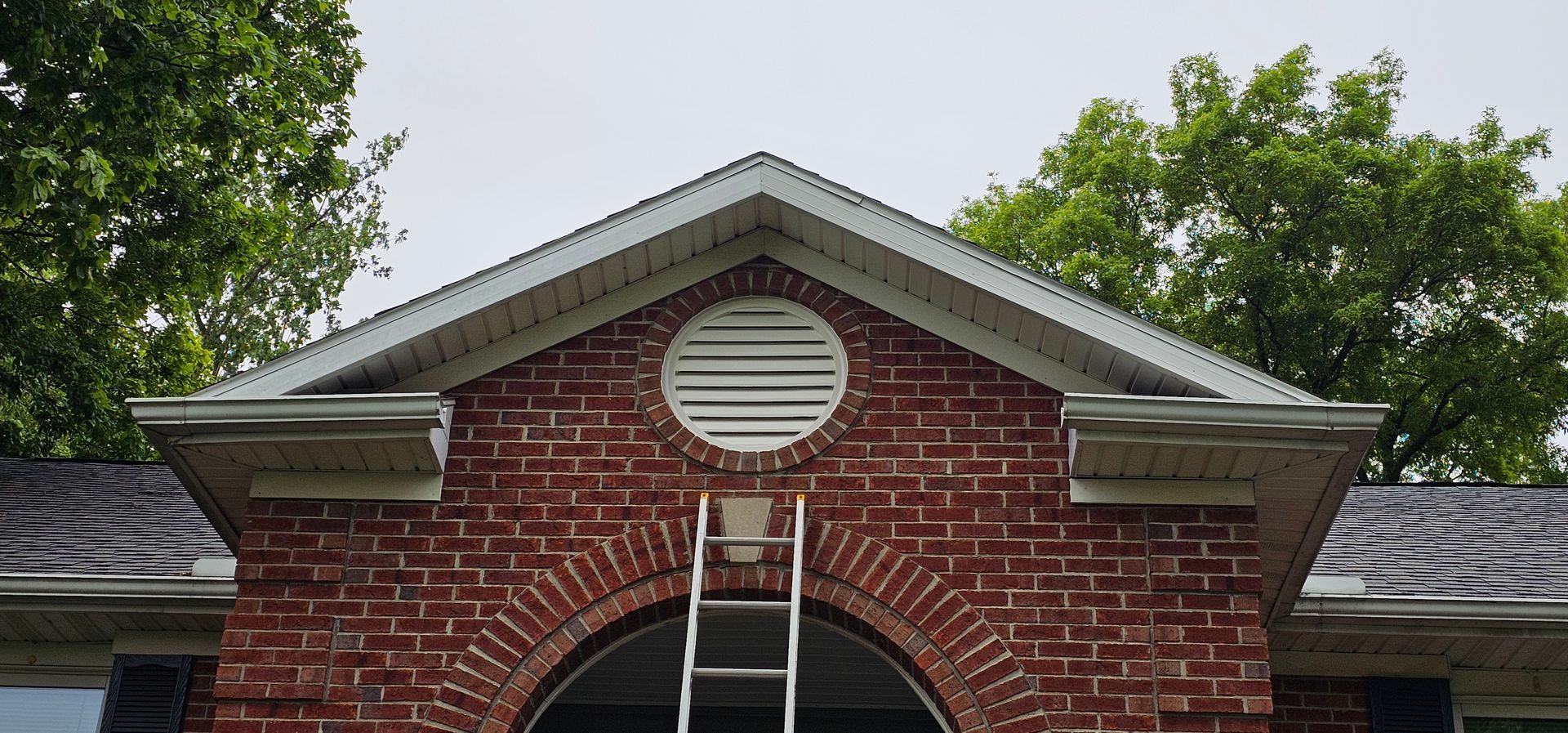 Brick house gable with round attic vent and a ladder leaning beneath it