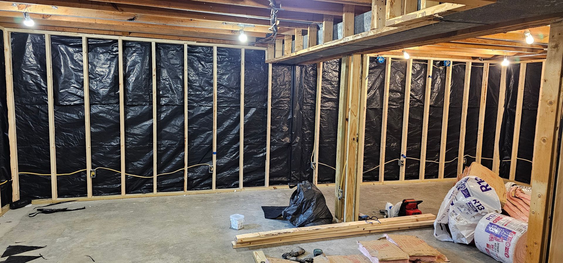 Unfinished basement with exposed wooden framing, insulation, and construction materials on the floor.