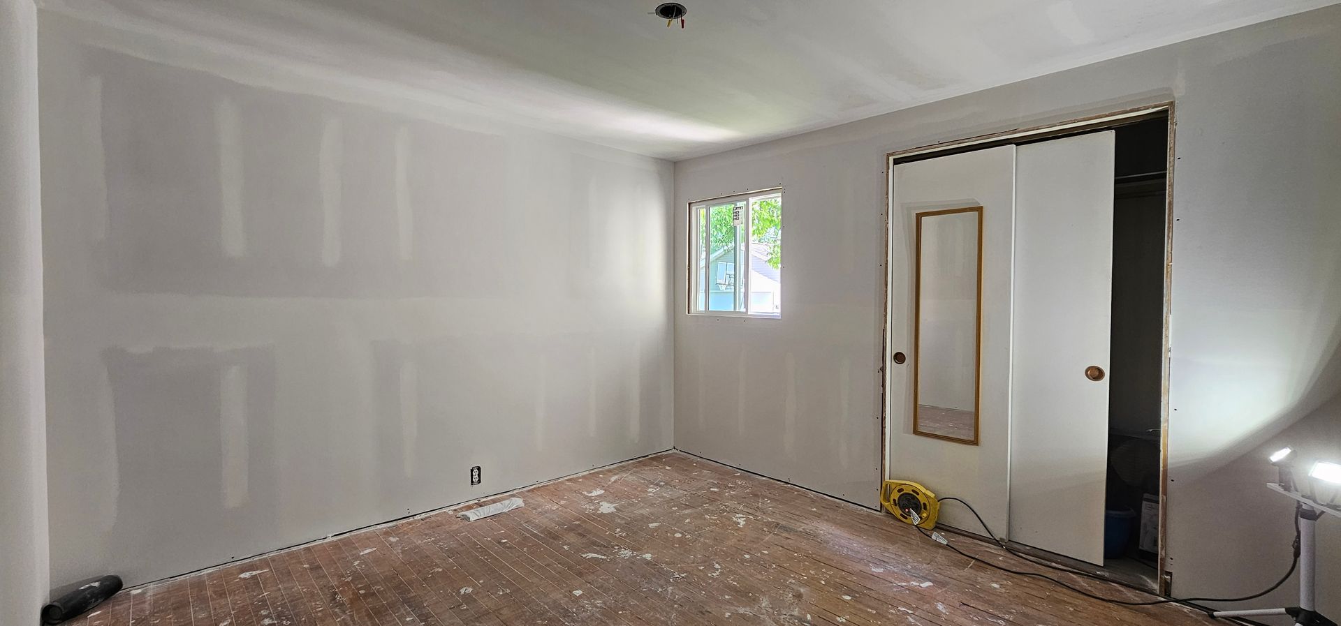 Empty unfinished bedroom with gray walls, bare floor, small window, and open door to a dark closet.