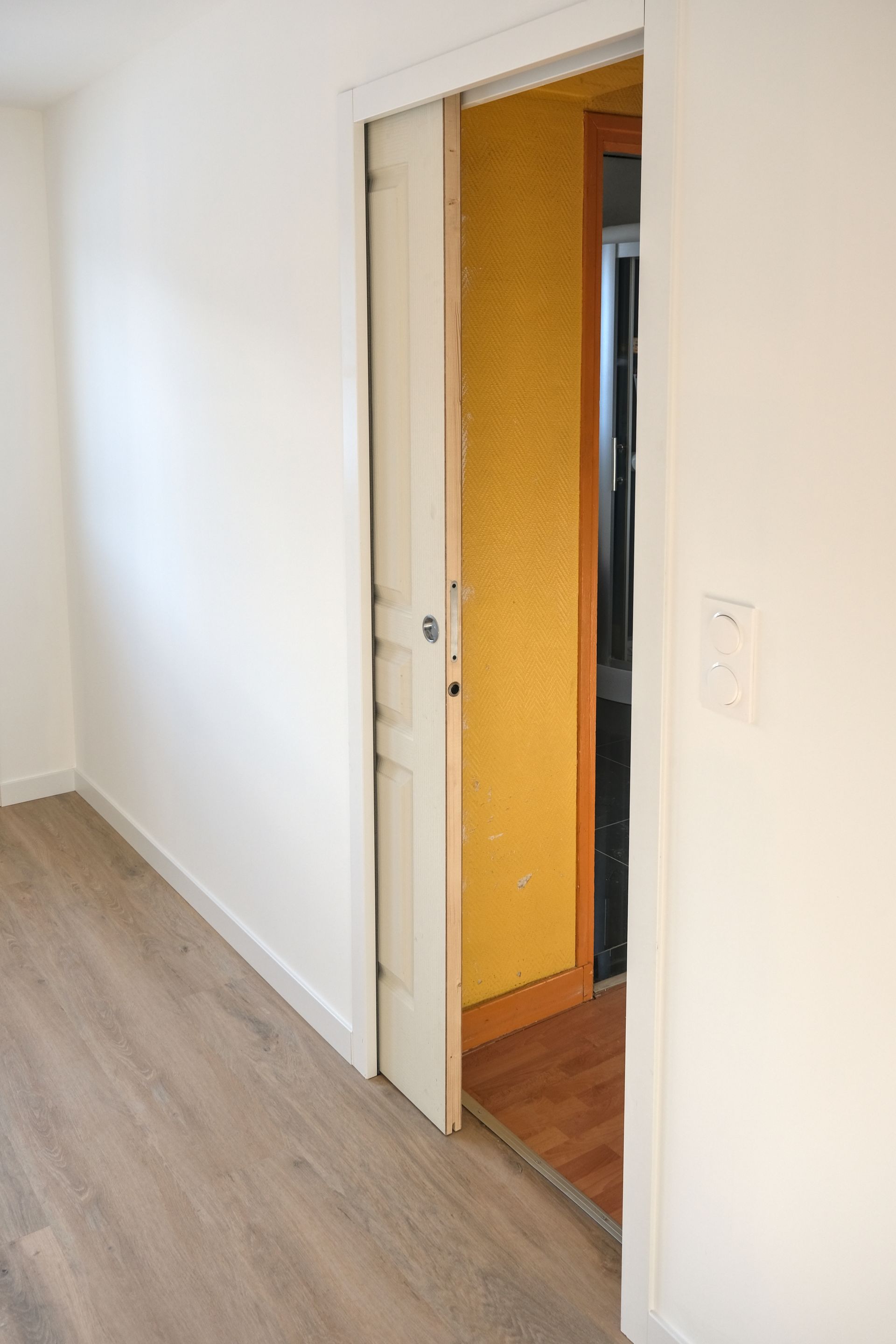 A hallway with a sliding door leading to a kitchen.