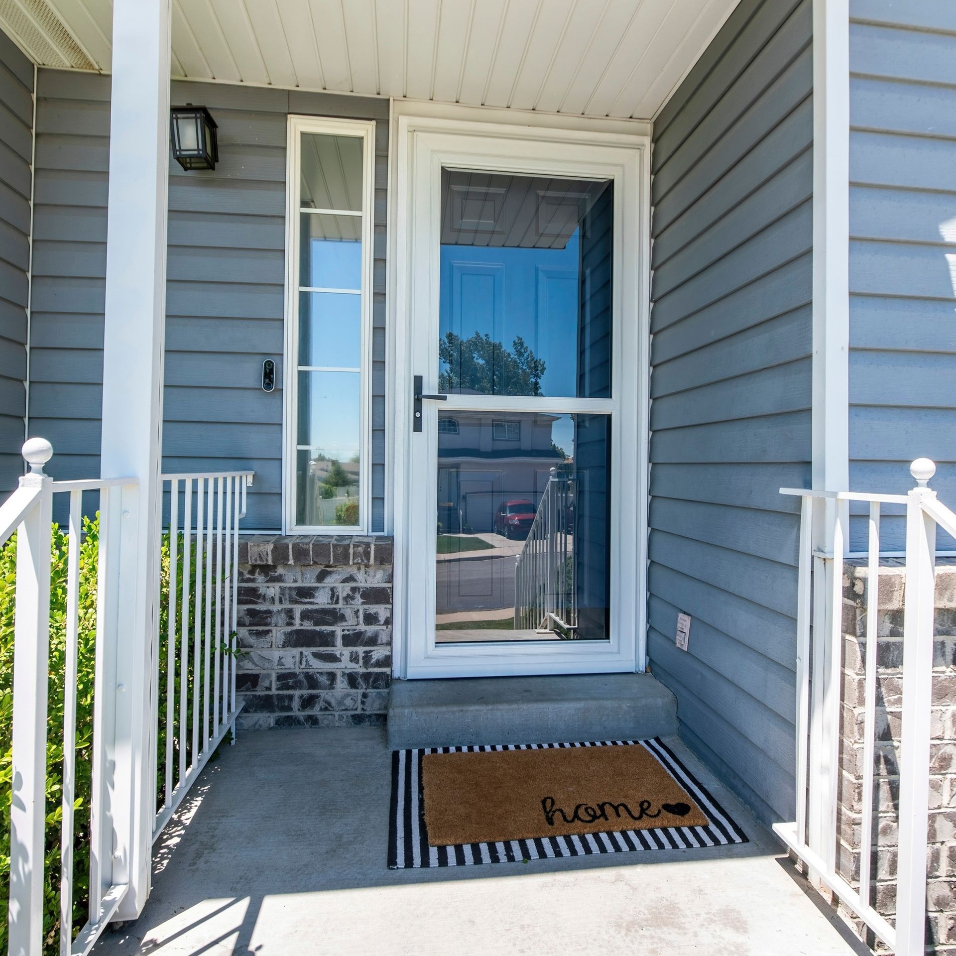 A man wearing a straw hat is installing a screen door on a brick sidewalk.