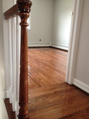 A wooden railing leading to an empty room with hardwood floors.
