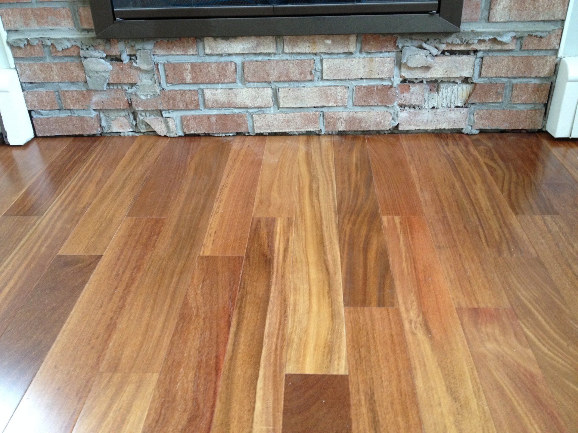 A wooden floor in front of a brick fireplace.